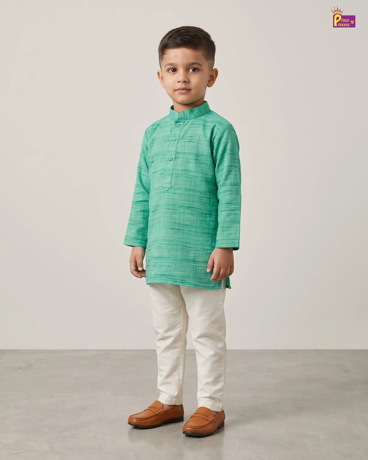 A young boy modeling a mint green textured kurta with cream trousers and brown leather shoes, standing against a neutral studio backdrop.