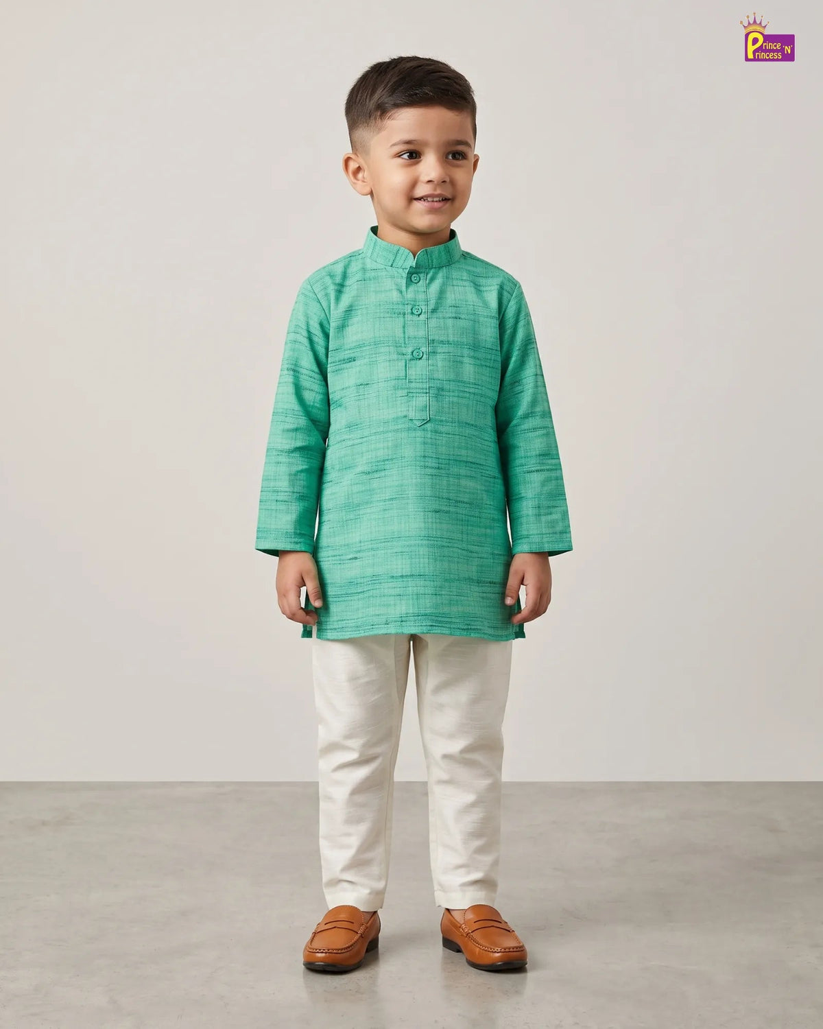 A young boy modeling a mint green textured long-sleeve kurta with white trousers and brown leather loafers, standing against a neutral light gray studio background.