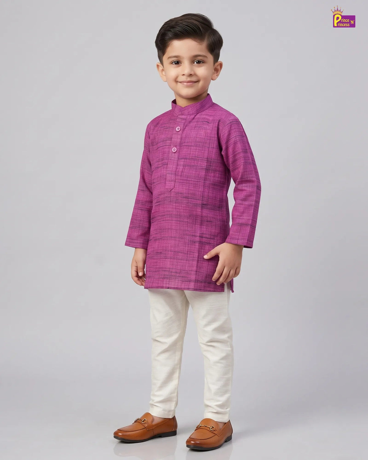 A young boy modeling a magenta purple long-sleeve kurta with a subtle grid pattern, paired with off-white trousers and brown leather loafers, against a solid gray studio background.