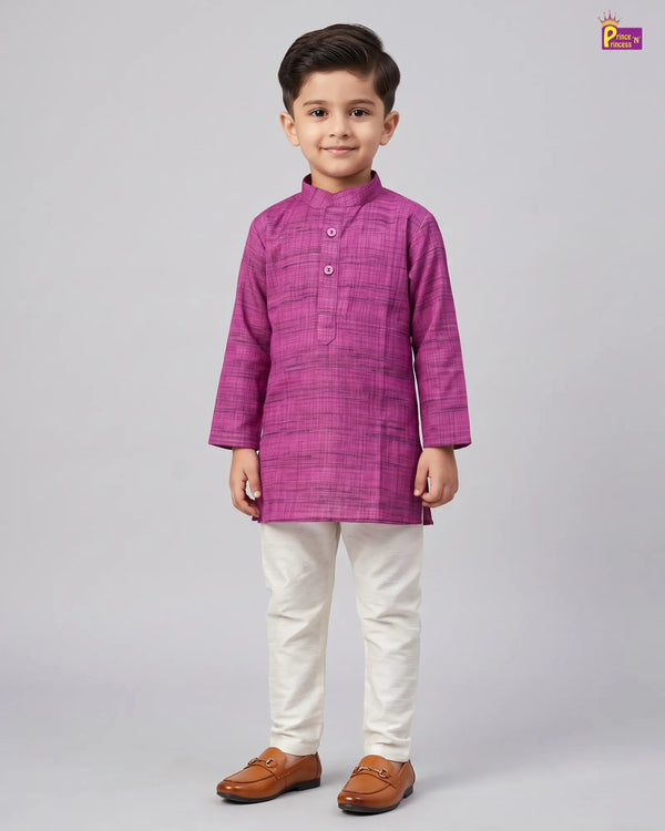 A young boy modeling a magenta purple long-sleeve kurta with a subtle grid pattern, paired with off-white trousers and brown leather loafers, shot against a solid gray studio background.