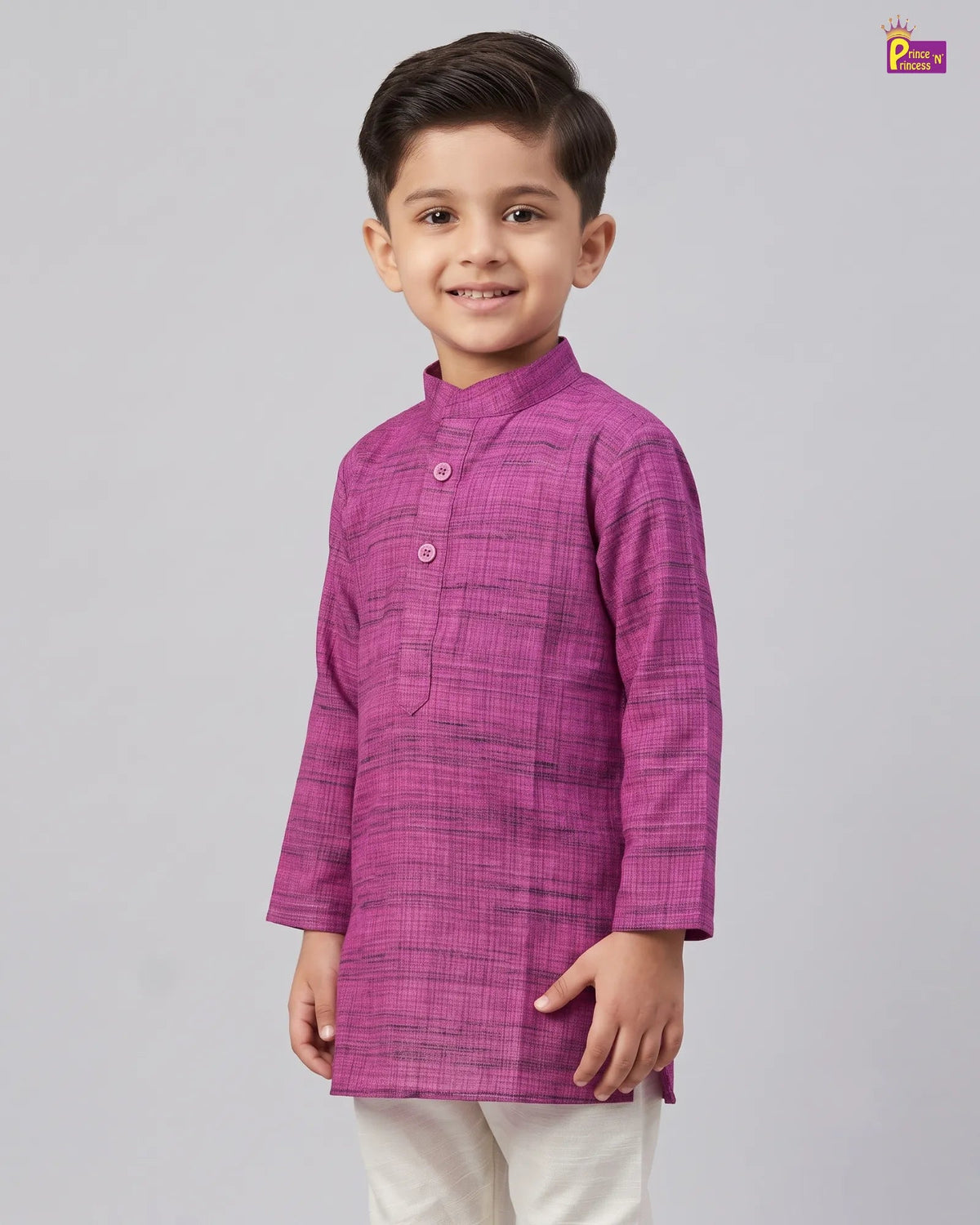 A young boy wearing a magenta purple textured kurta with white trousers, standing against a solid gray studio background.