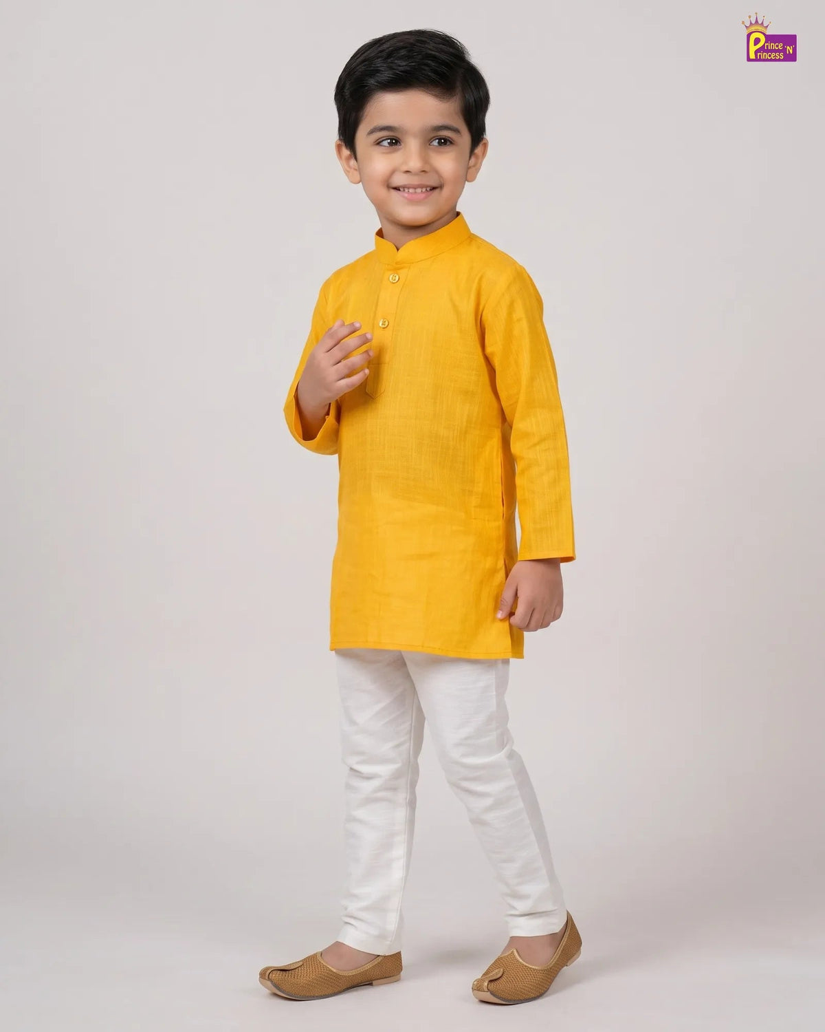 A young boy modeling a bright yellow kurta with white trousers and brown shoes, standing against a light gray studio background.