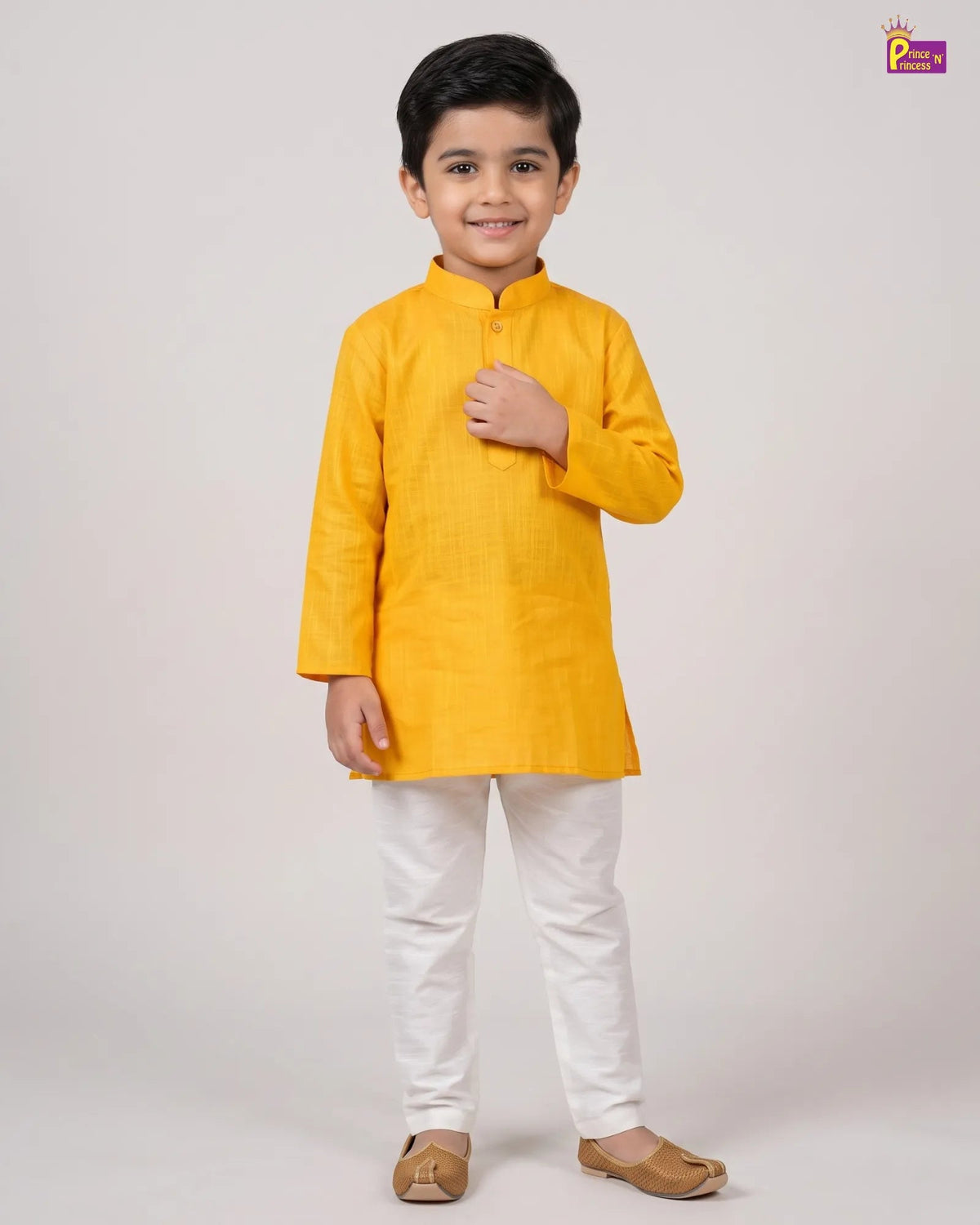 A young boy modeling a bright yellow kurta with white trousers and brown sandals, standing against a plain light gray studio background.