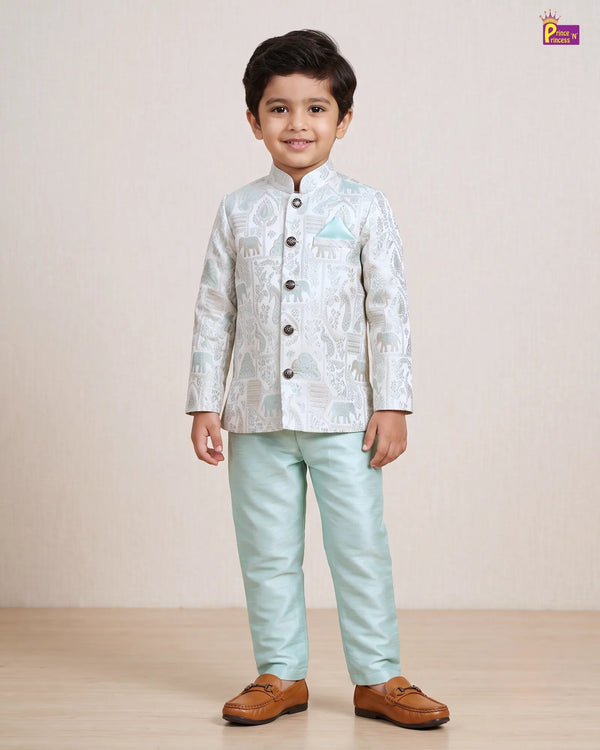 A young boy modeling a traditional Indian outfit consisting of a light blue and white patterned sherwani jacket with dark buttons, paired with light mint green trousers and brown leather loafers, standing against a neutral beige background.
