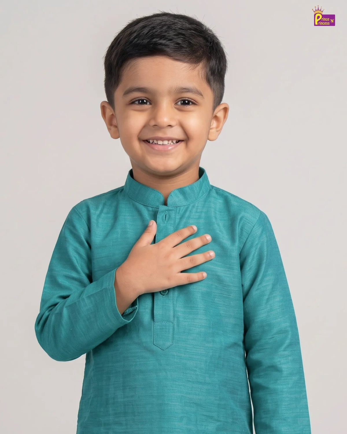 A young boy smiling and wearing a teal long-sleeve kurta with a mandarin collar, standing against a light gray background.