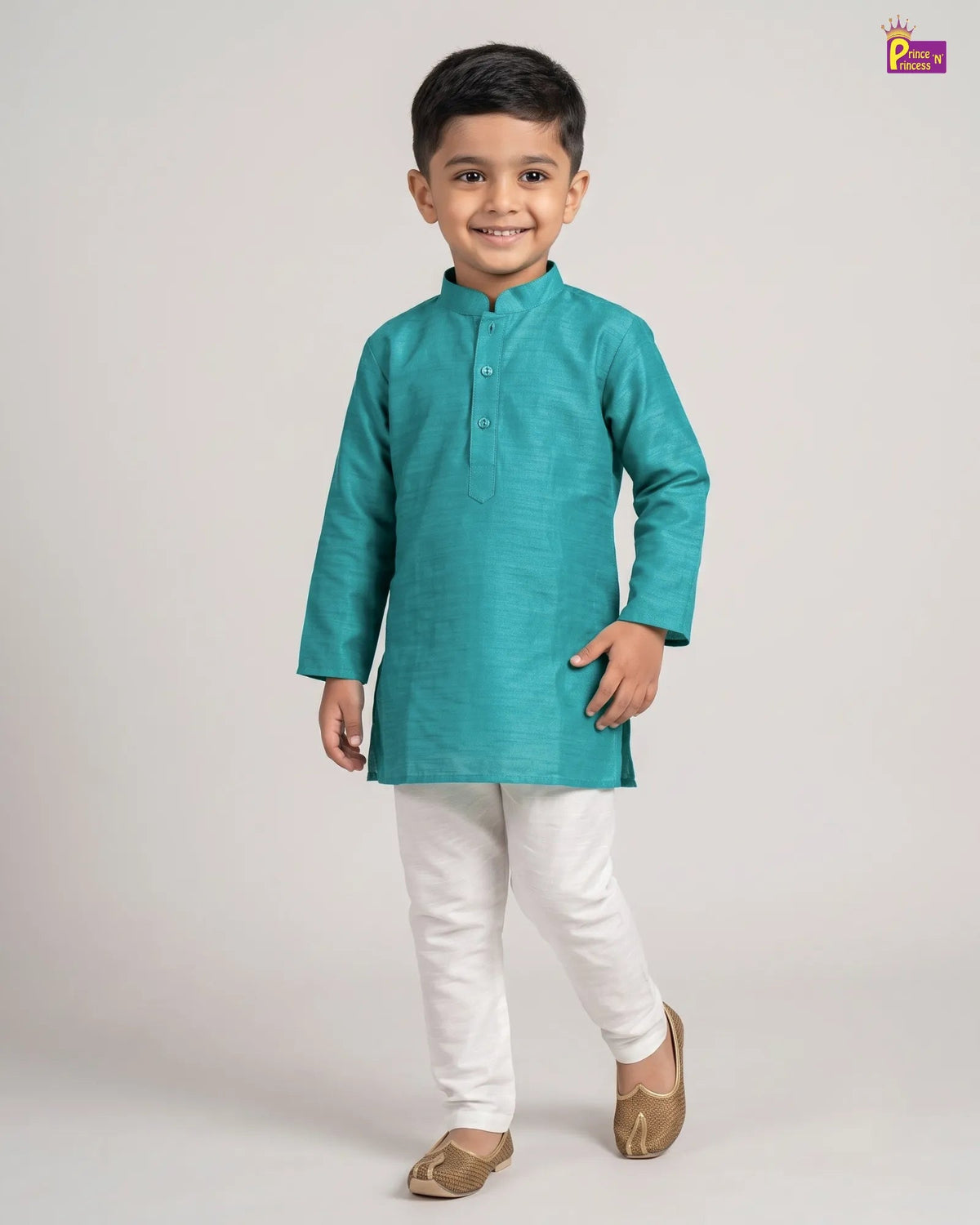 A young boy modeling a teal green long-sleeve kurta with white trousers and brown shoes, standing against a light gray studio background.