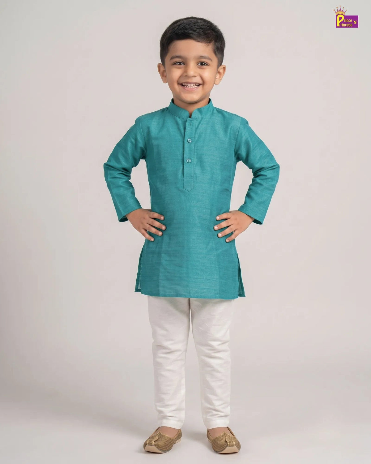 A young boy modeling a teal green long-sleeve kurta with white trousers and beige shoes, standing against a light gray studio background.