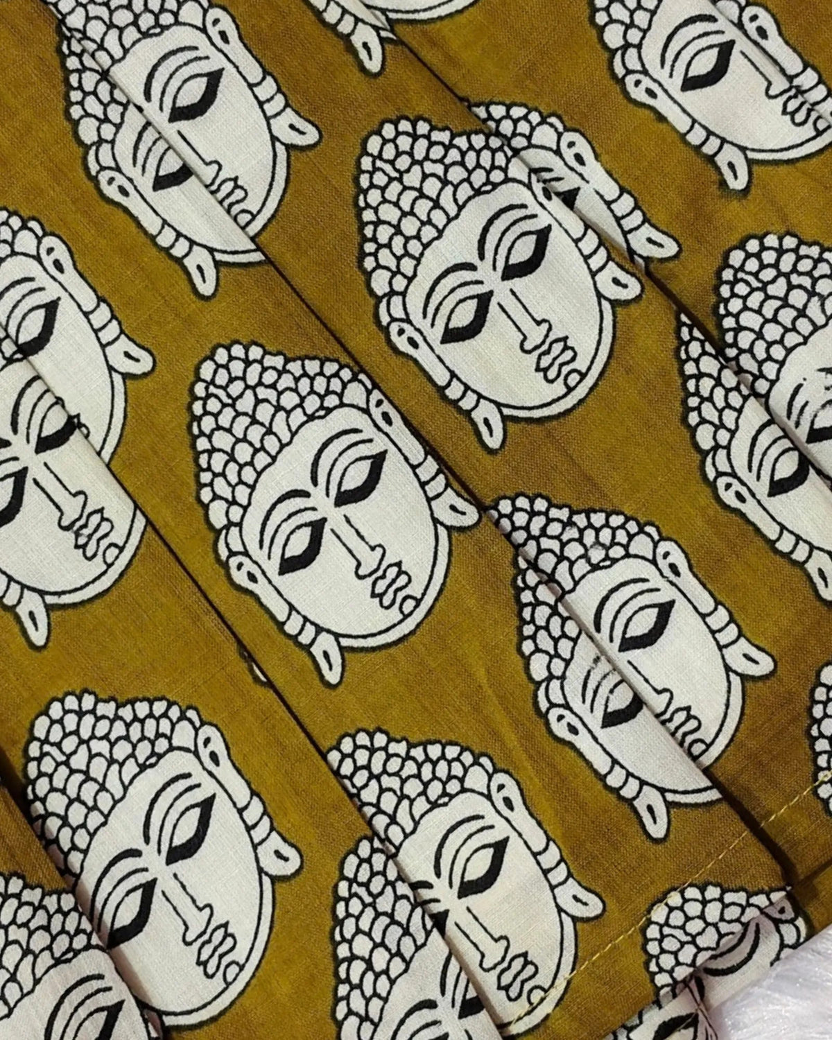 A close-up of a fabric pattern featuring a repeating design of Buddha heads in black and white on a mustard yellow background.