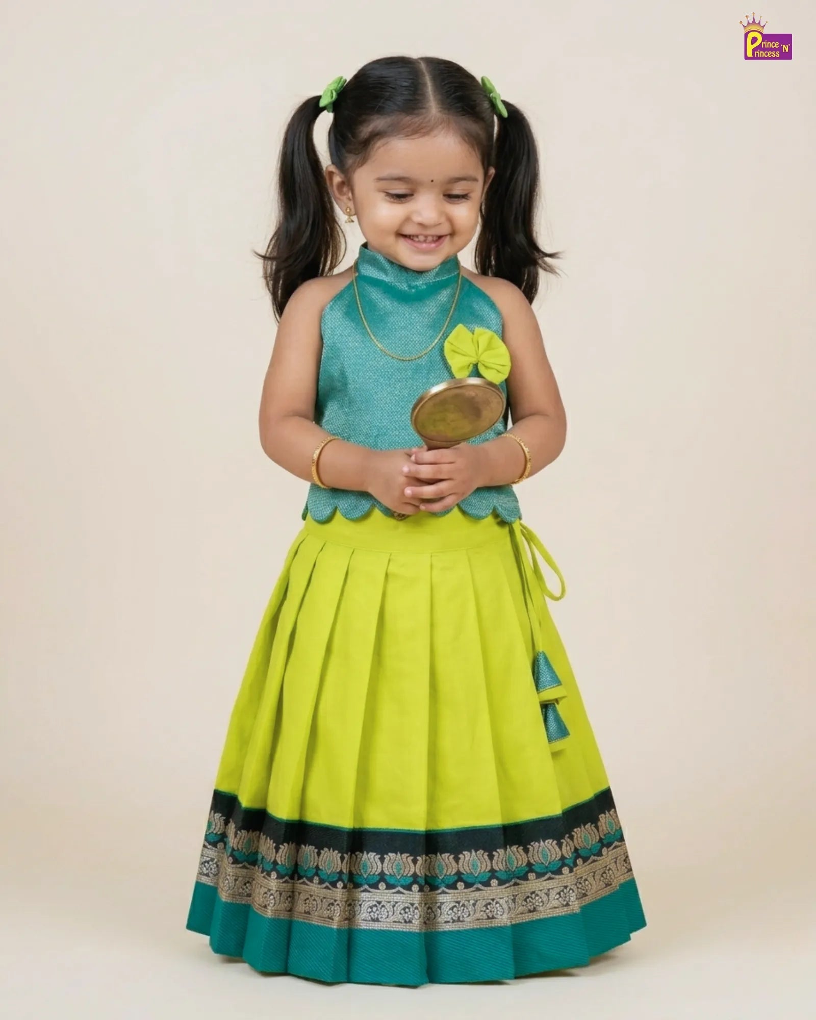 Young girl wearing a green and yellow traditional outfit holding a decorative item.