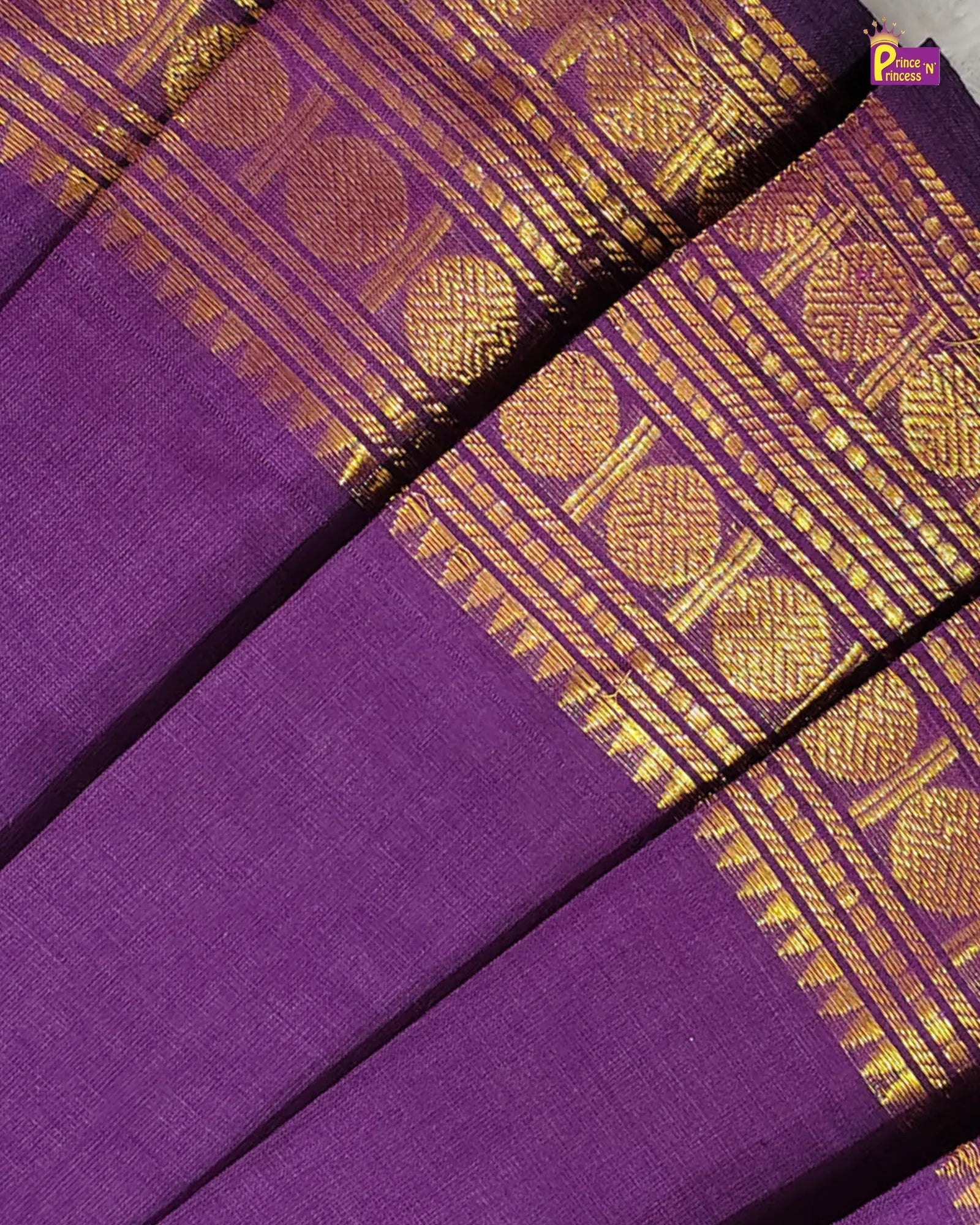 Purple silk saree fabric with a wide gold zari brocade border featuring traditional circular and geometric motifs.