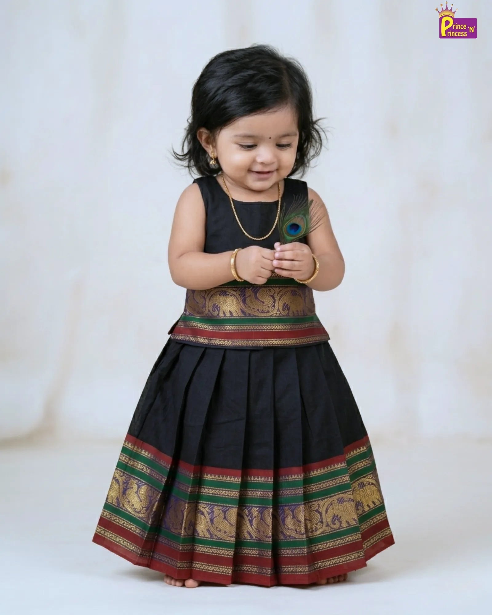 Child wearing a traditional black dress with colorful patterns on a white background