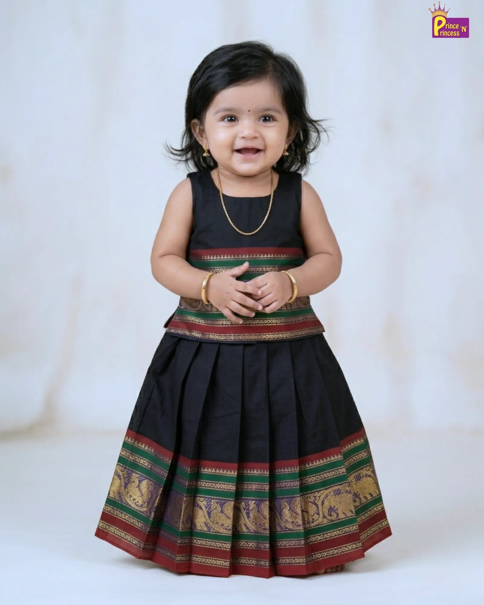 Child wearing a traditional black dress with colorful patterns on a white background