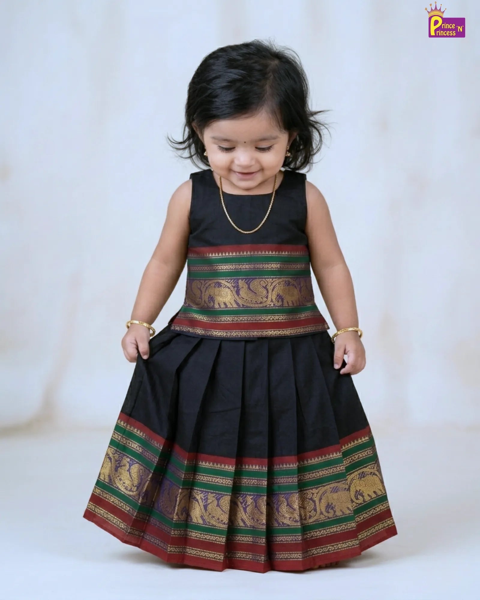 Child wearing a traditional black dress with colorful patterns on a white background