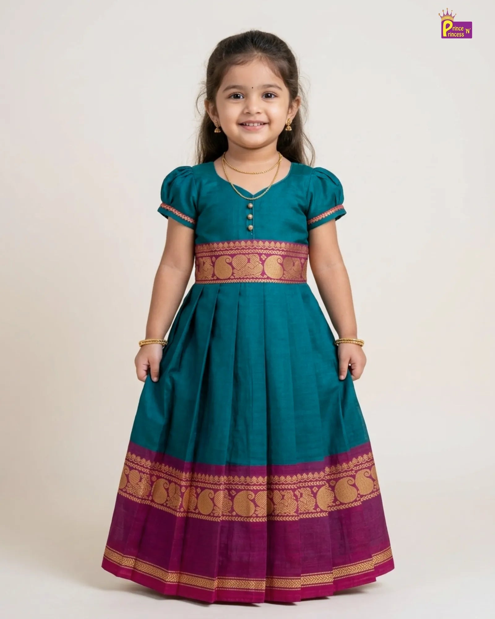Young girl wearing a teal and purple traditional dress with gold patterns on a white background