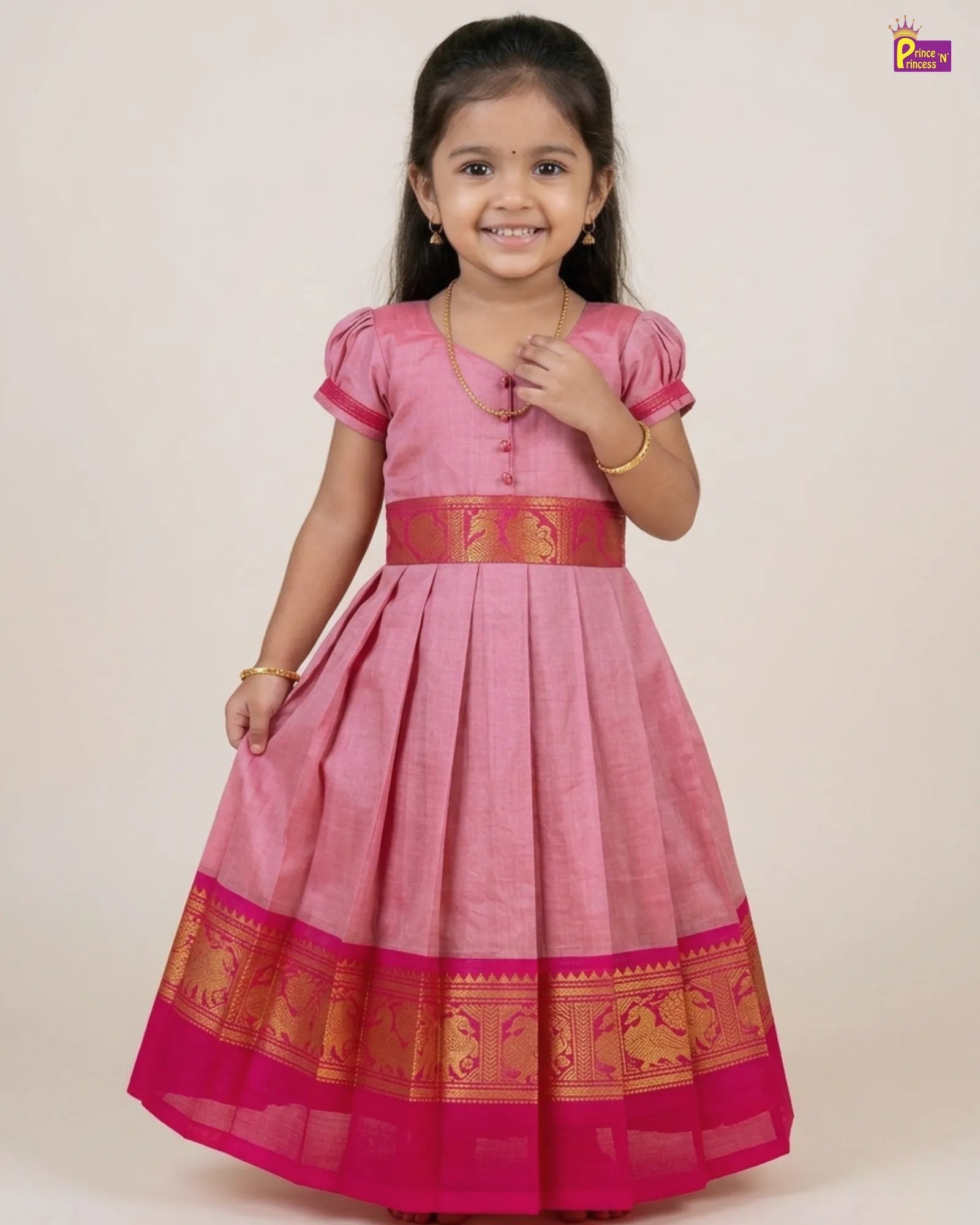 Young girl wearing a pink traditional outfit with gold accents on a plain background
