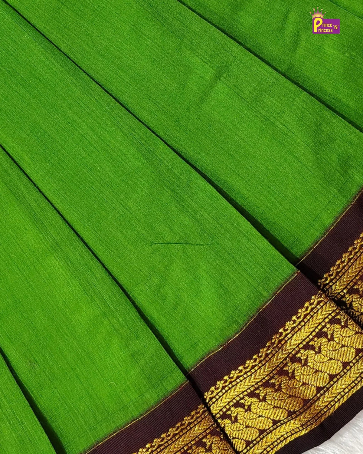 A close-up of a bright green silk saree with a dark brown border featuring intricate gold zari embroidery.