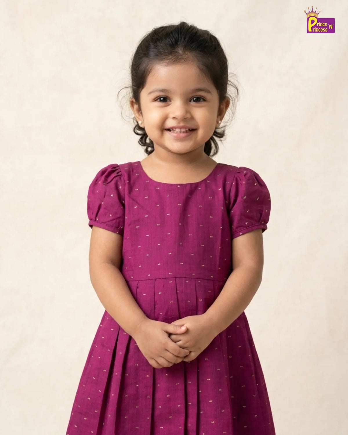 A young girl with dark hair tied back is wearing a magenta purple short-sleeve dress with a small white pattern, standing against a textured beige background. A 'Place of Pride' logo is visible in the top right corner.