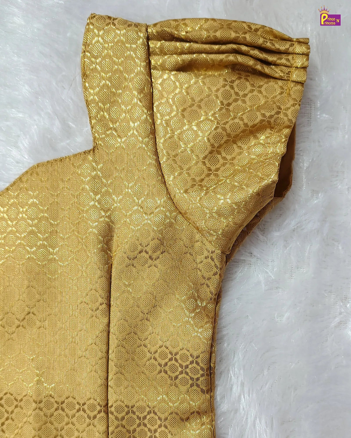 A close-up of a gold brocade fabric with a repeating geometric pattern, draped on a white faux fur background.