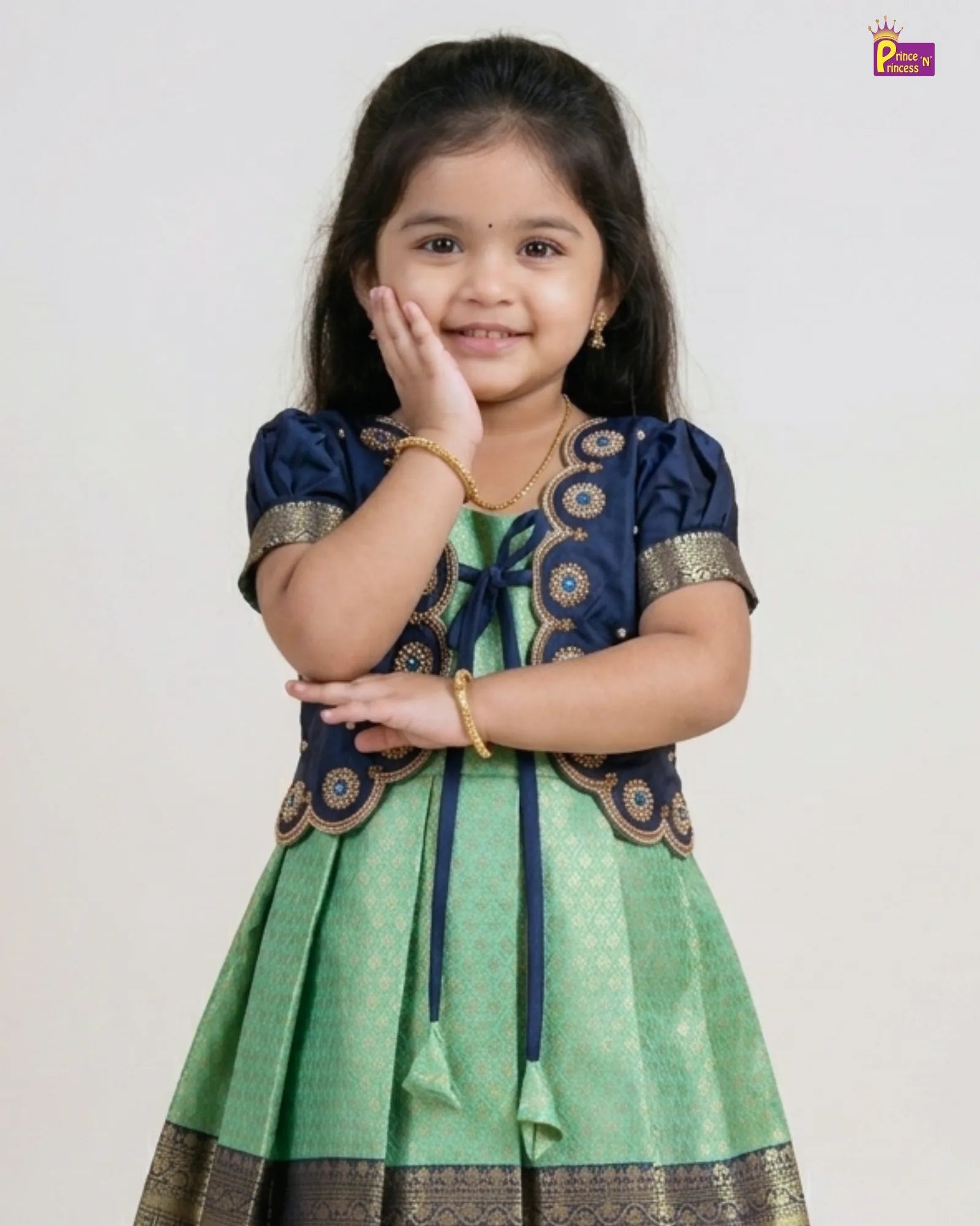 Young girl wearing a green and blue traditional outfit with gold accents on a white background