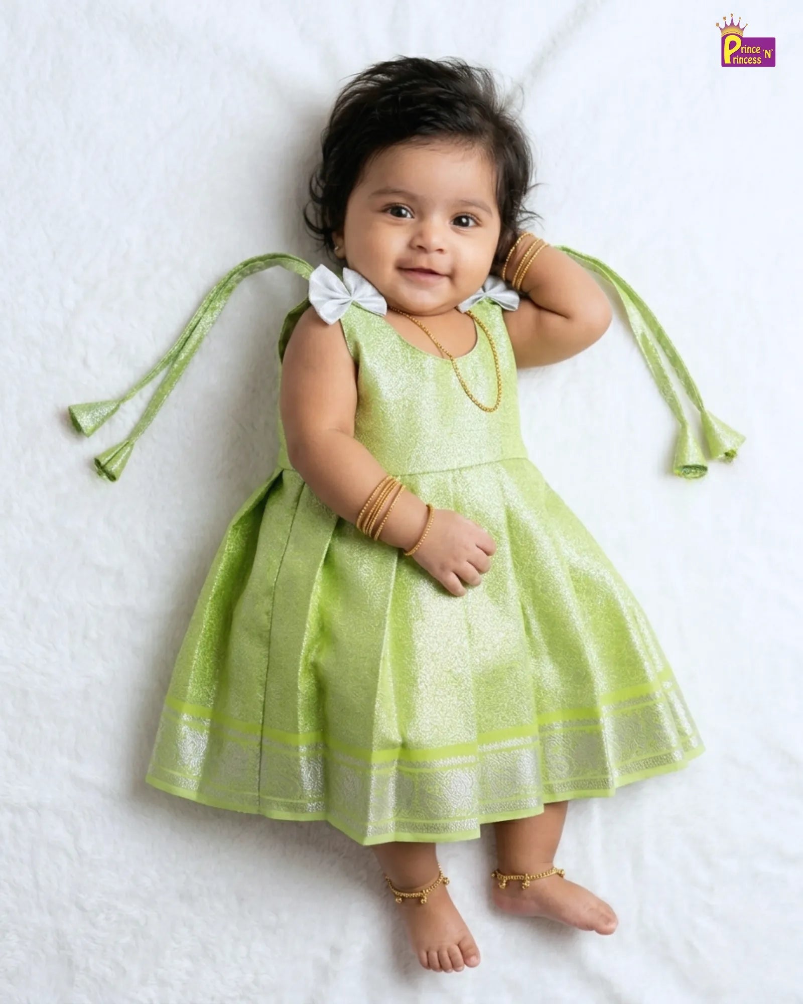 Baby wearing a green dress with decorative straps on a white background