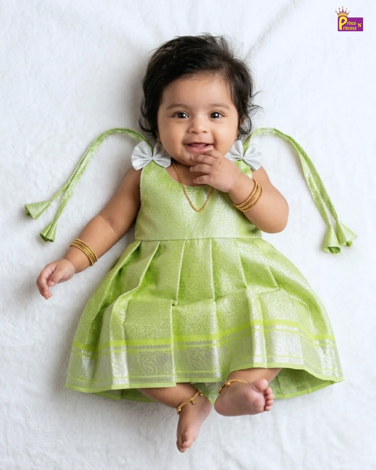 Baby in a green dress lying on a white surface