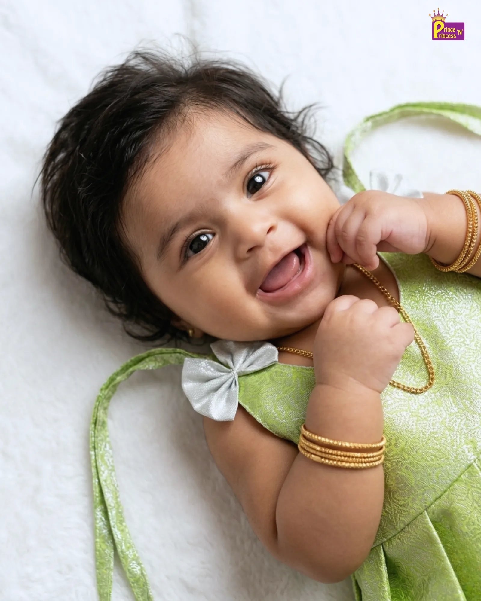 Baby in a green outfit with gold bangles on a white background