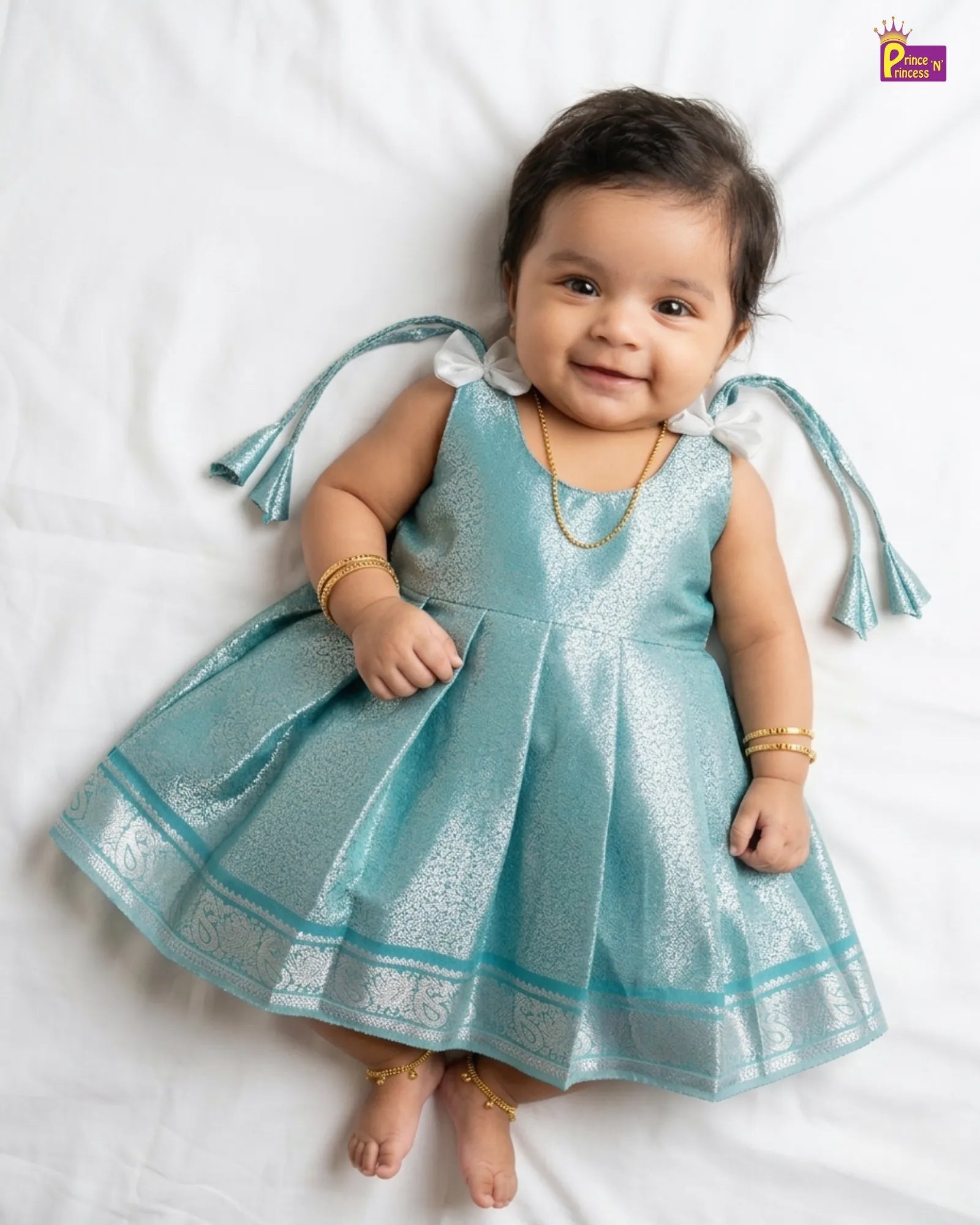 Baby wearing a blue dress with tassels on a white background