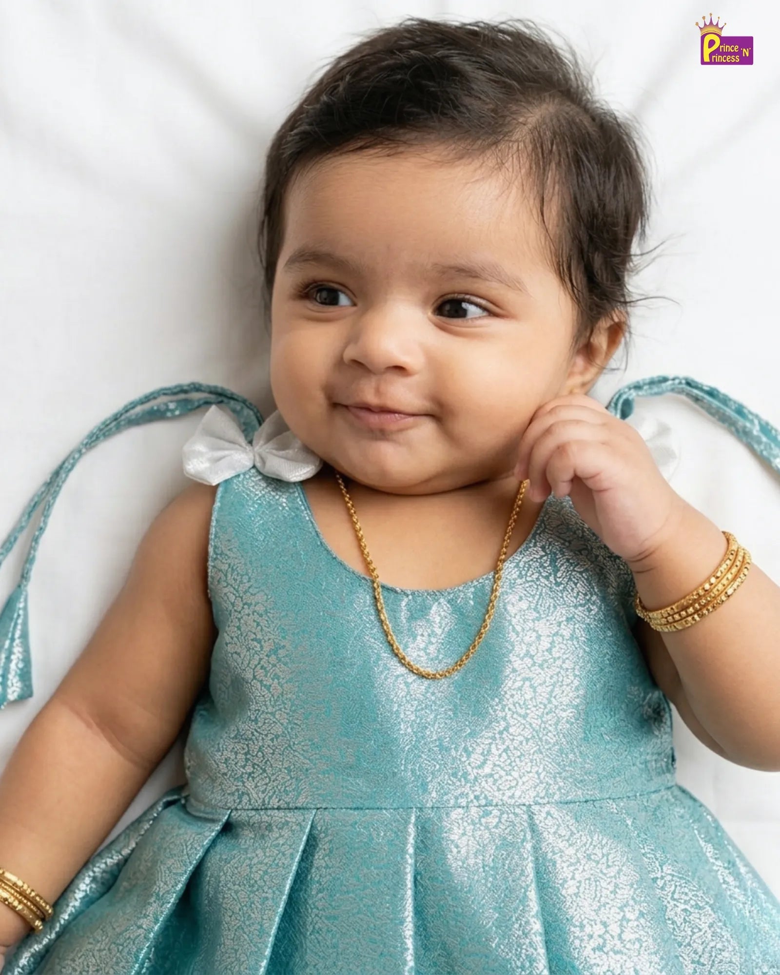 Baby in a blue dress with gold jewelry on a white background