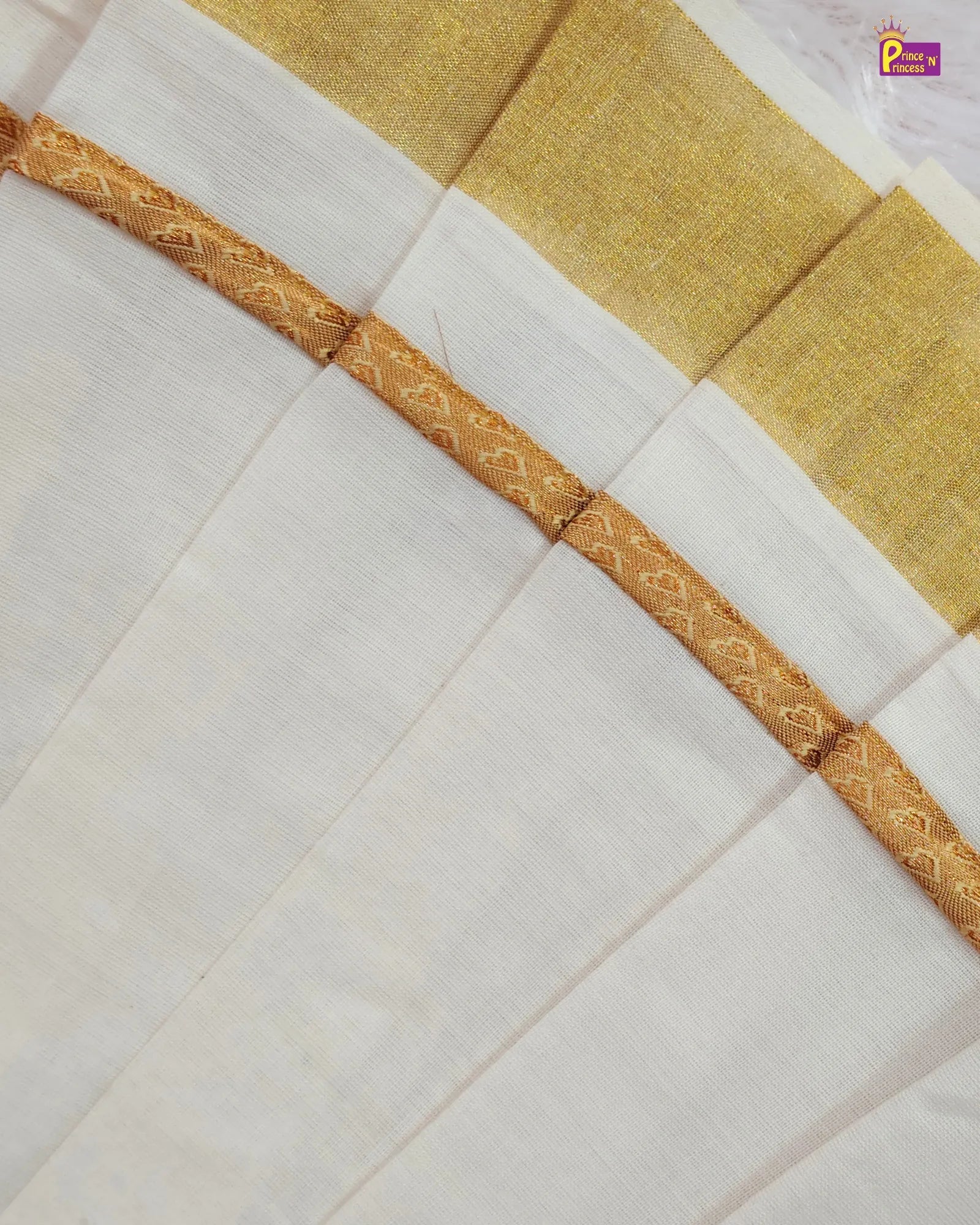 A close-up of a white silk saree with a gold zari border and a gold pallu section, showing the fine texture of the fabric and the metallic embroidery.