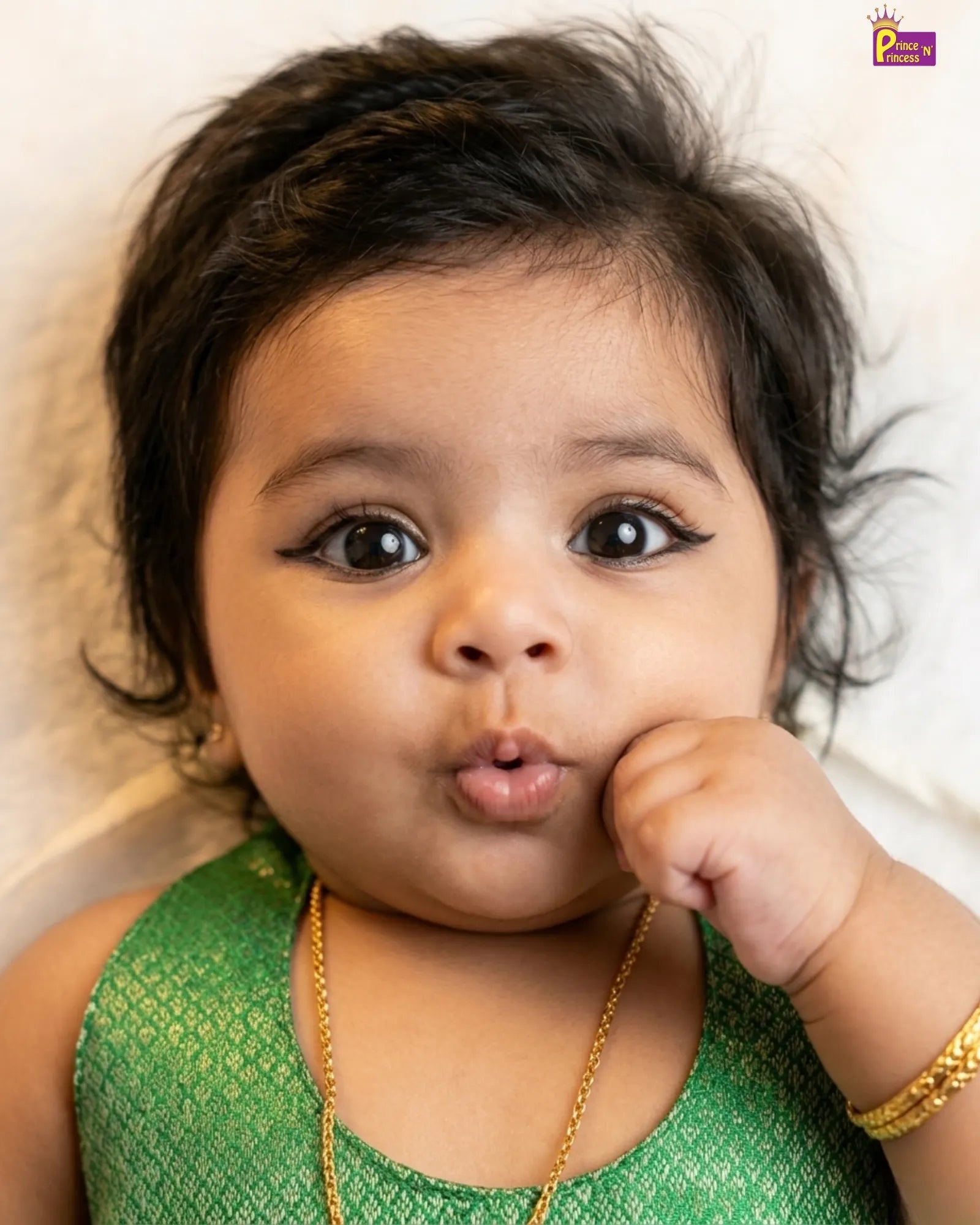 Baby in a green outfit with gold jewelry on a light background