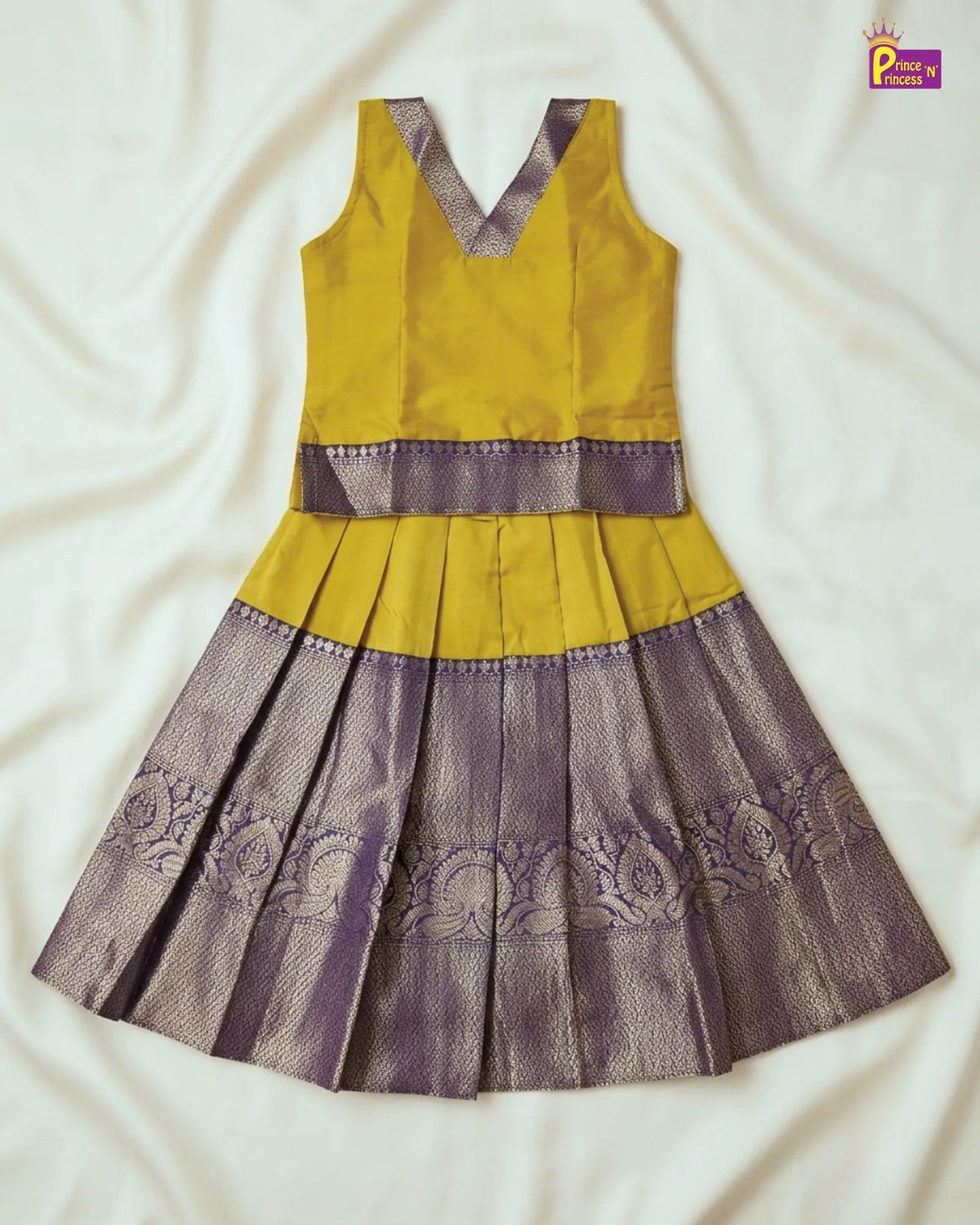 A sleeveless traditional dress with a mustard yellow top and a pleated skirt in metallic lavender-purple with floral embroidery, laid flat on a white fabric background.