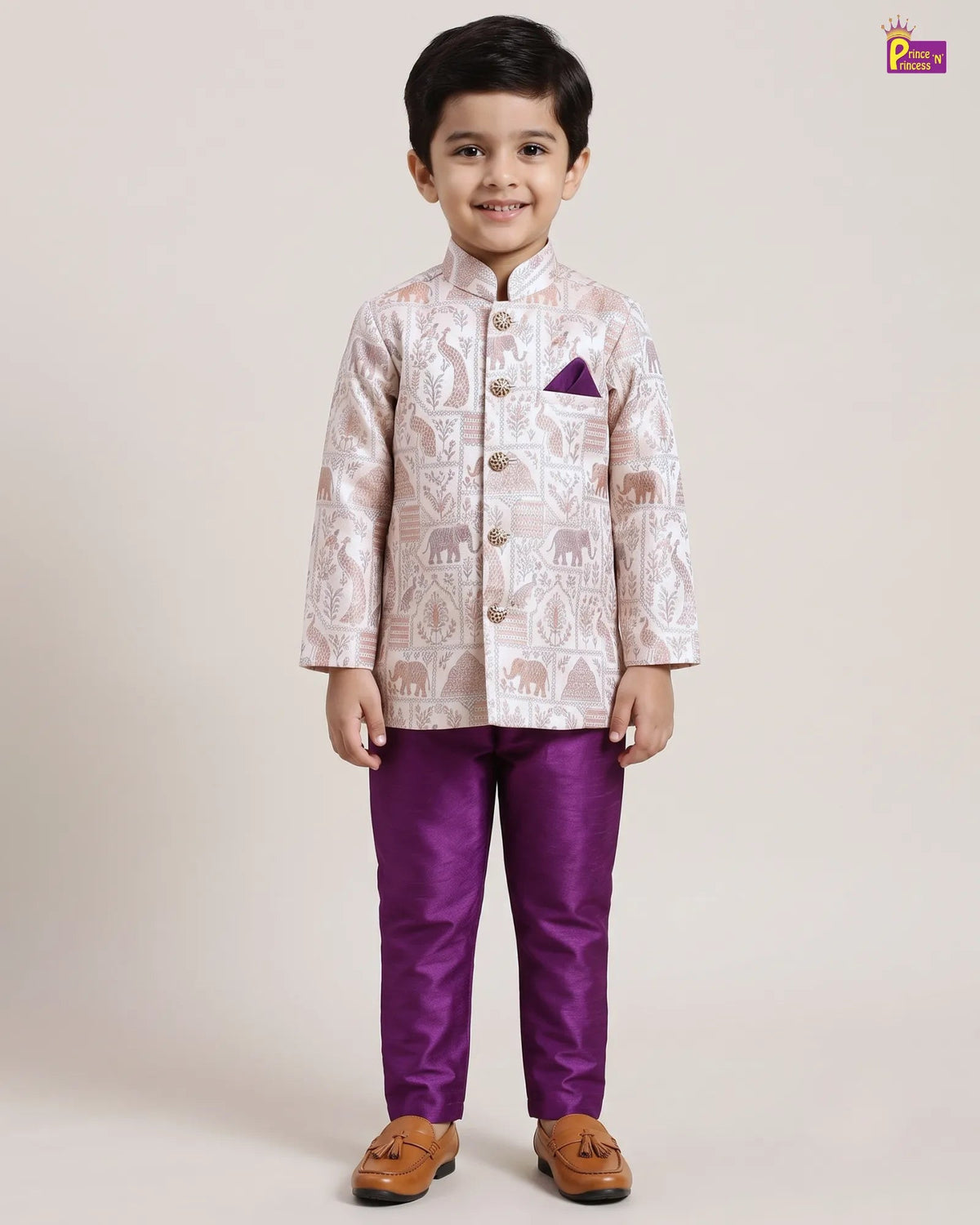 A young boy modeling a traditional Indian outfit consisting of a light beige and white patterned sherwani jacket with a purple pocket square, paired with solid purple trousers and brown tassel shoes, against a plain beige studio background.