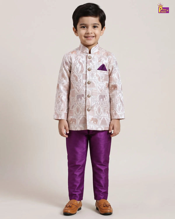 A young boy modeling a traditional Indian outfit consisting of a light beige and white patterned sherwani jacket with a purple pocket square, paired with solid purple trousers and brown tassel shoes, against a plain beige studio background.
