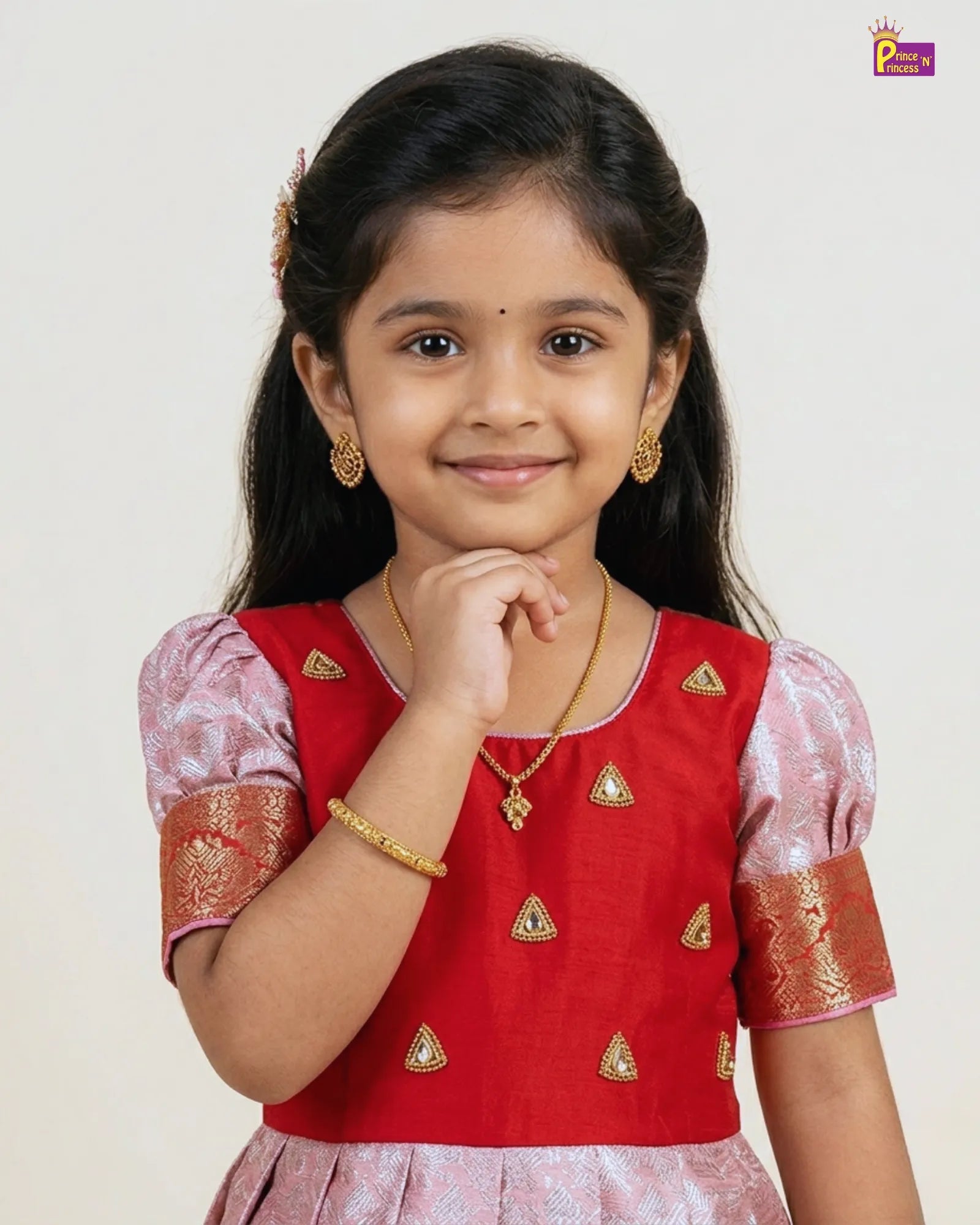 Young girl wearing a red and pink traditional outfit with gold jewelry on a white background