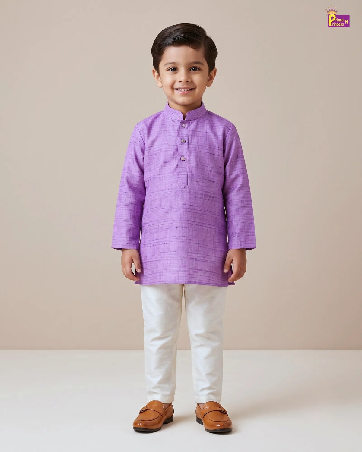 A young boy modeling a purple textured kurta with white trousers and brown leather shoes, standing against a solid beige studio background.
