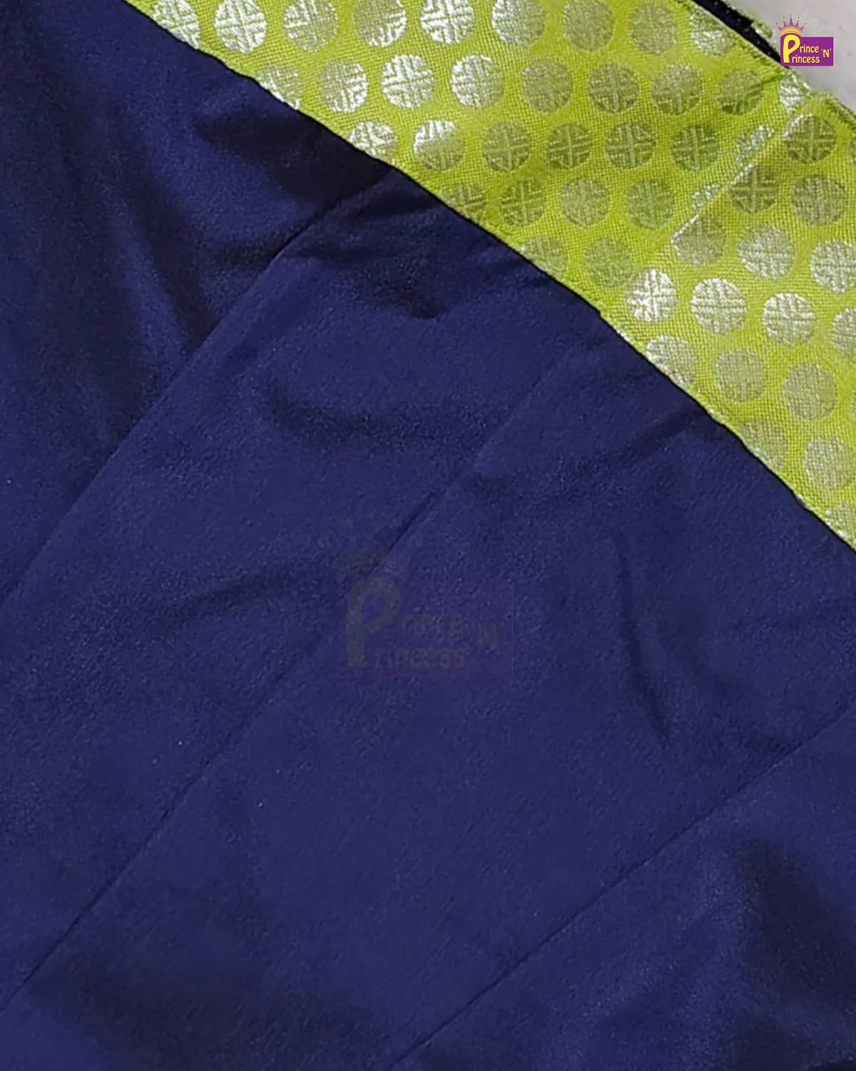A close-up of a dark navy blue fabric, likely silk, with a contrasting lime green border featuring a silver metallic geometric pattern.
