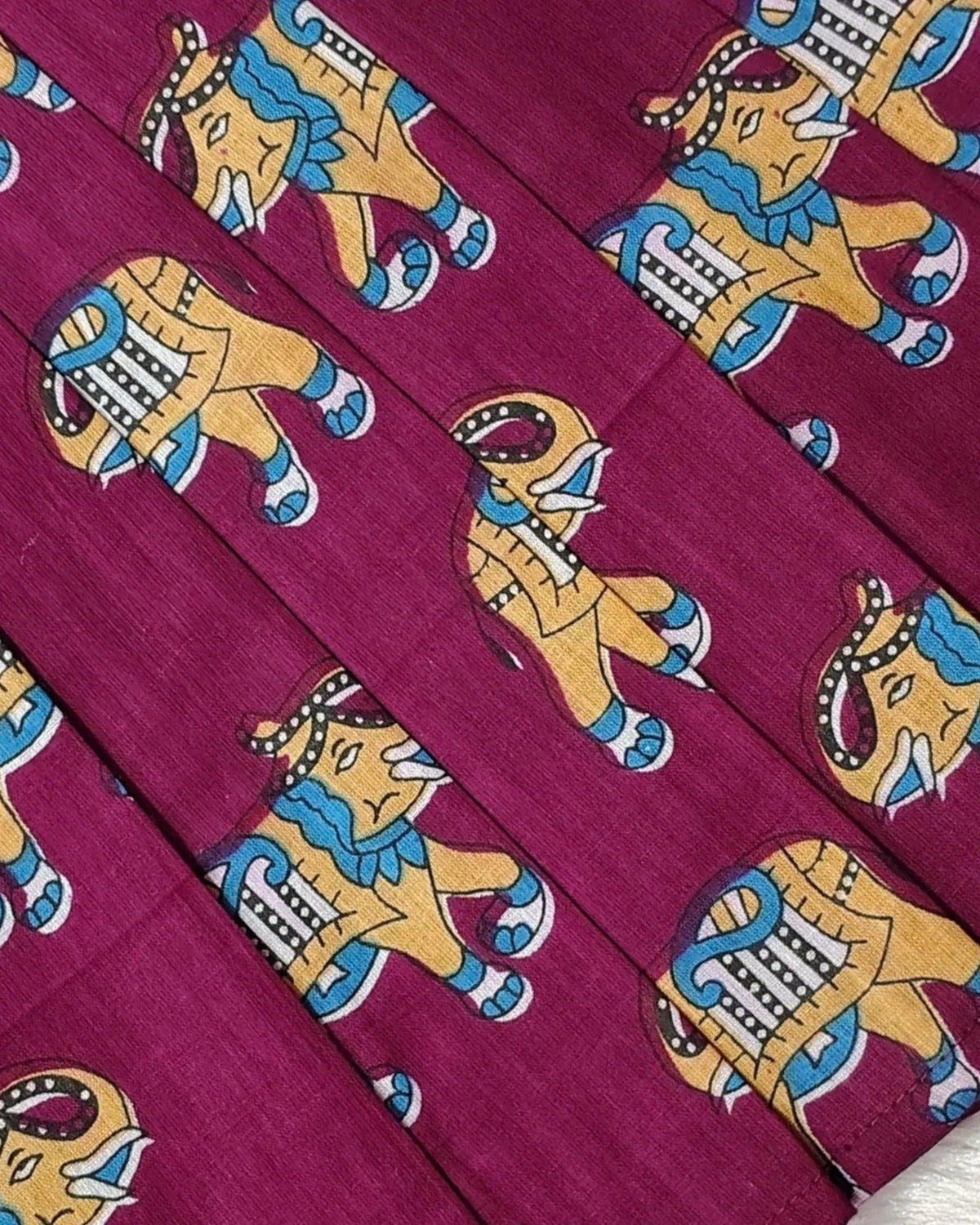 A close-up of a magenta fabric with a repeating print of stylized elephants in yellow, blue, and white.