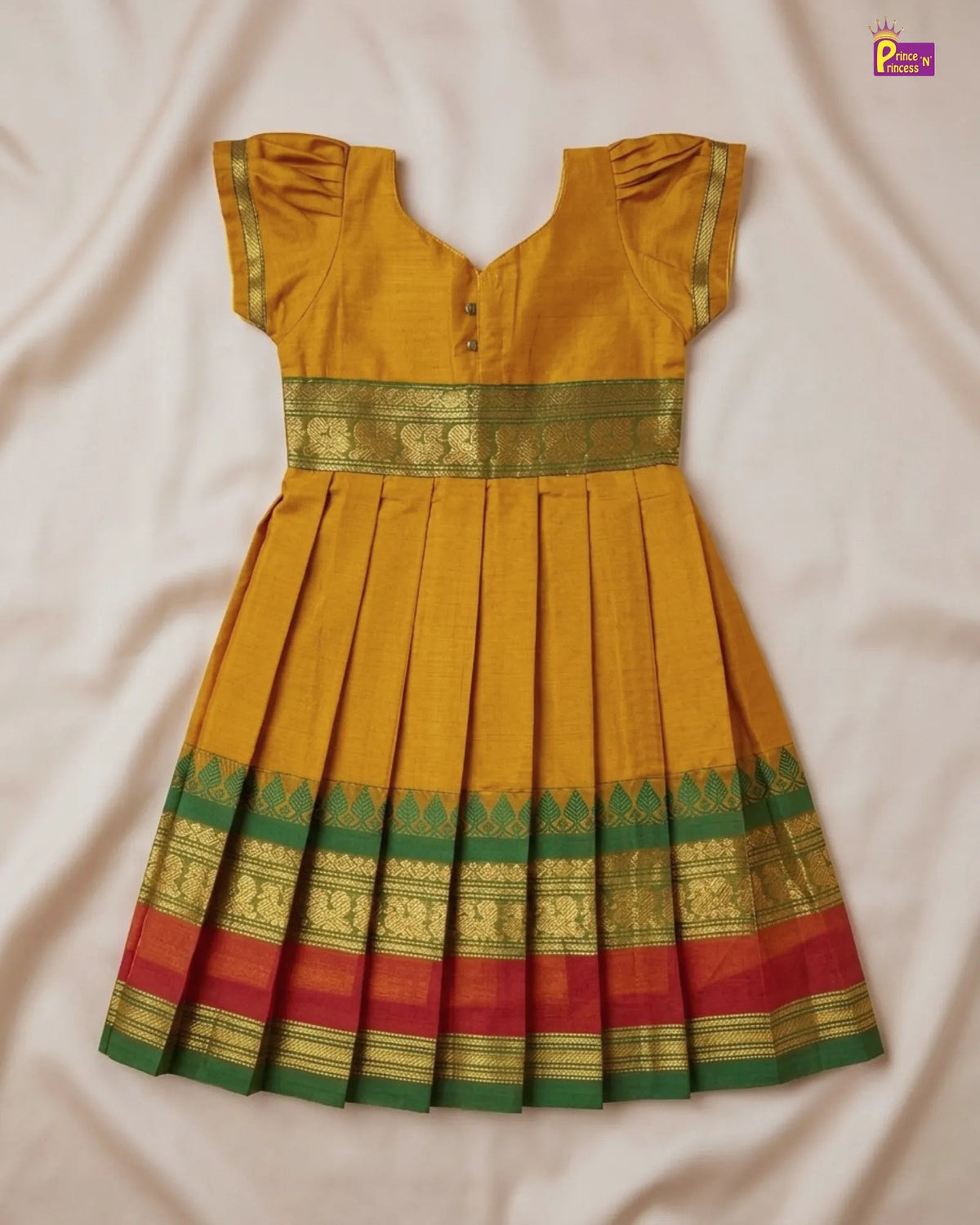 A mustard yellow traditional Indian dress with green and red zari borders, laid flat on a light beige fabric background.