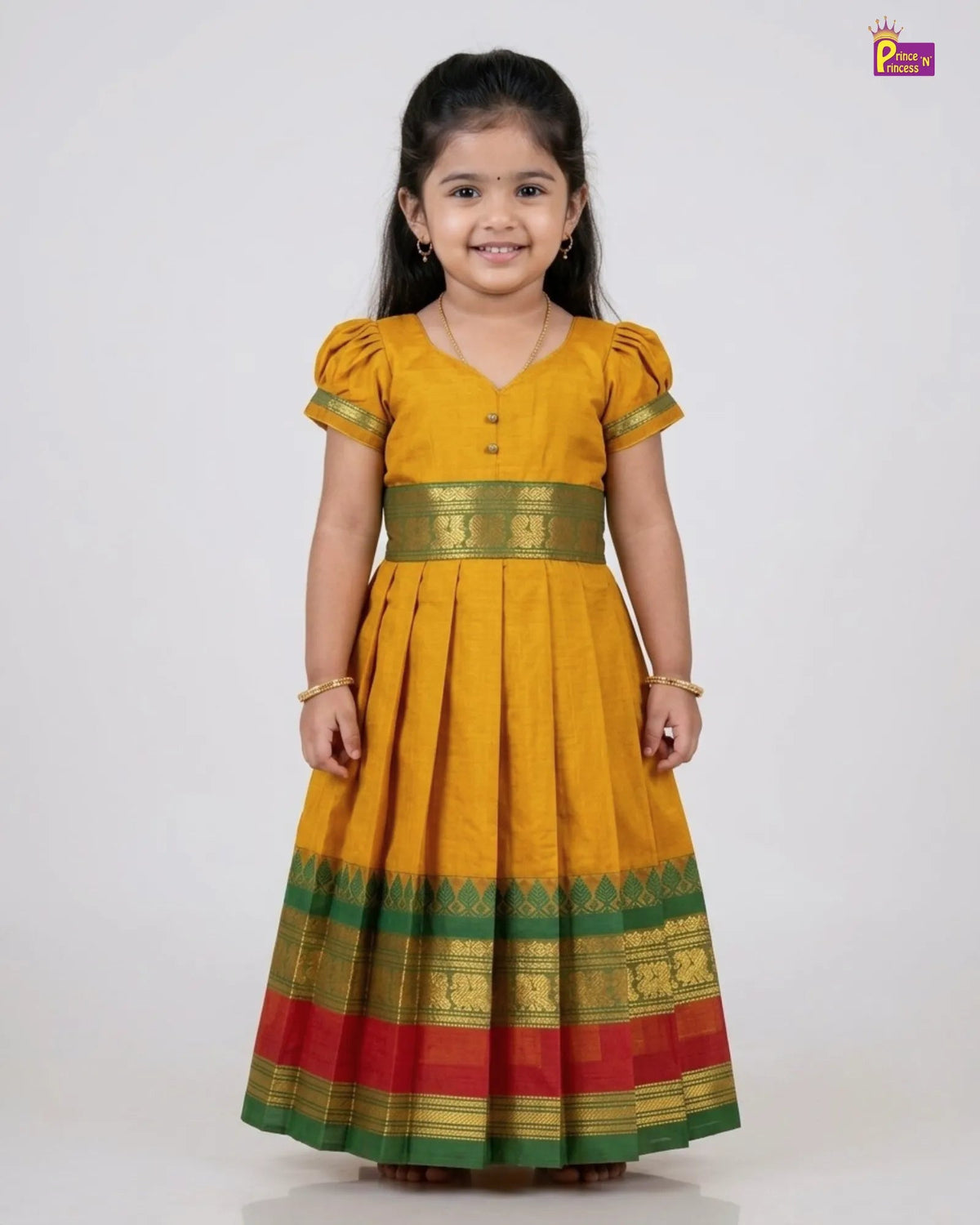 A young girl modeling a traditional Indian yellow kurta dress with green and red borders, standing against a plain white studio background.