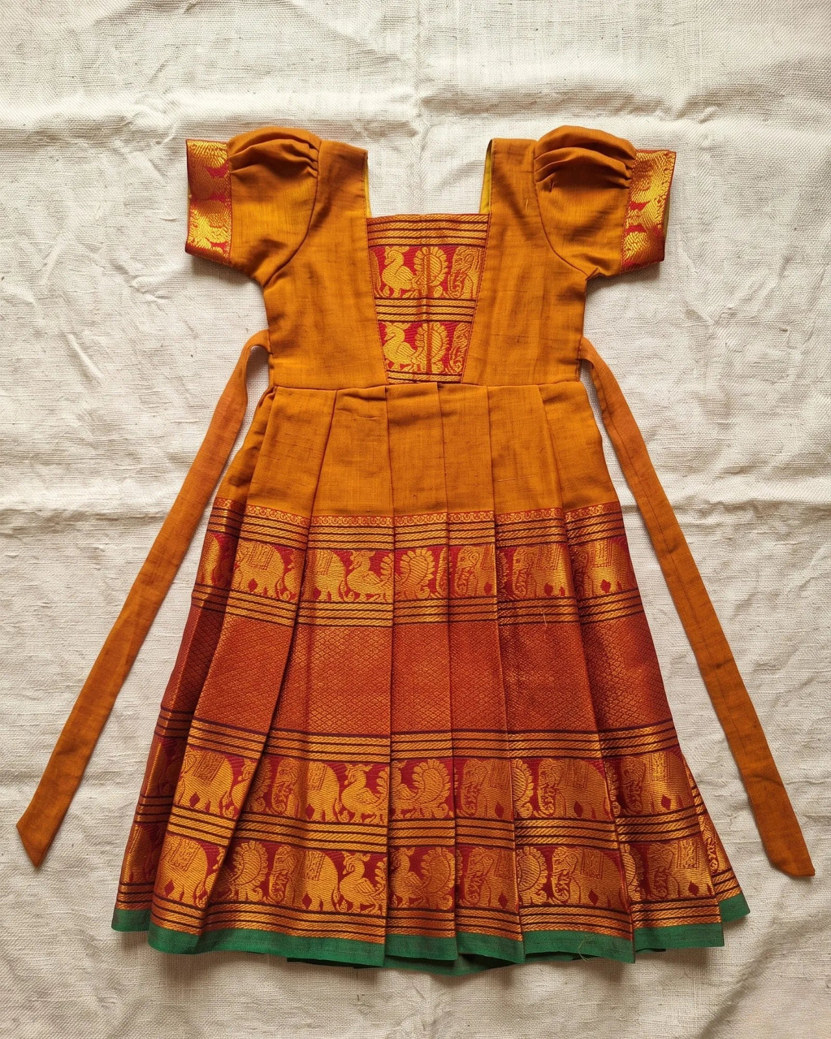 A traditional Indian kurta dress in mustard yellow and red, featuring a red elephant motif printed on the lower half and a green border at the hem, laid flat on a white fabric background.