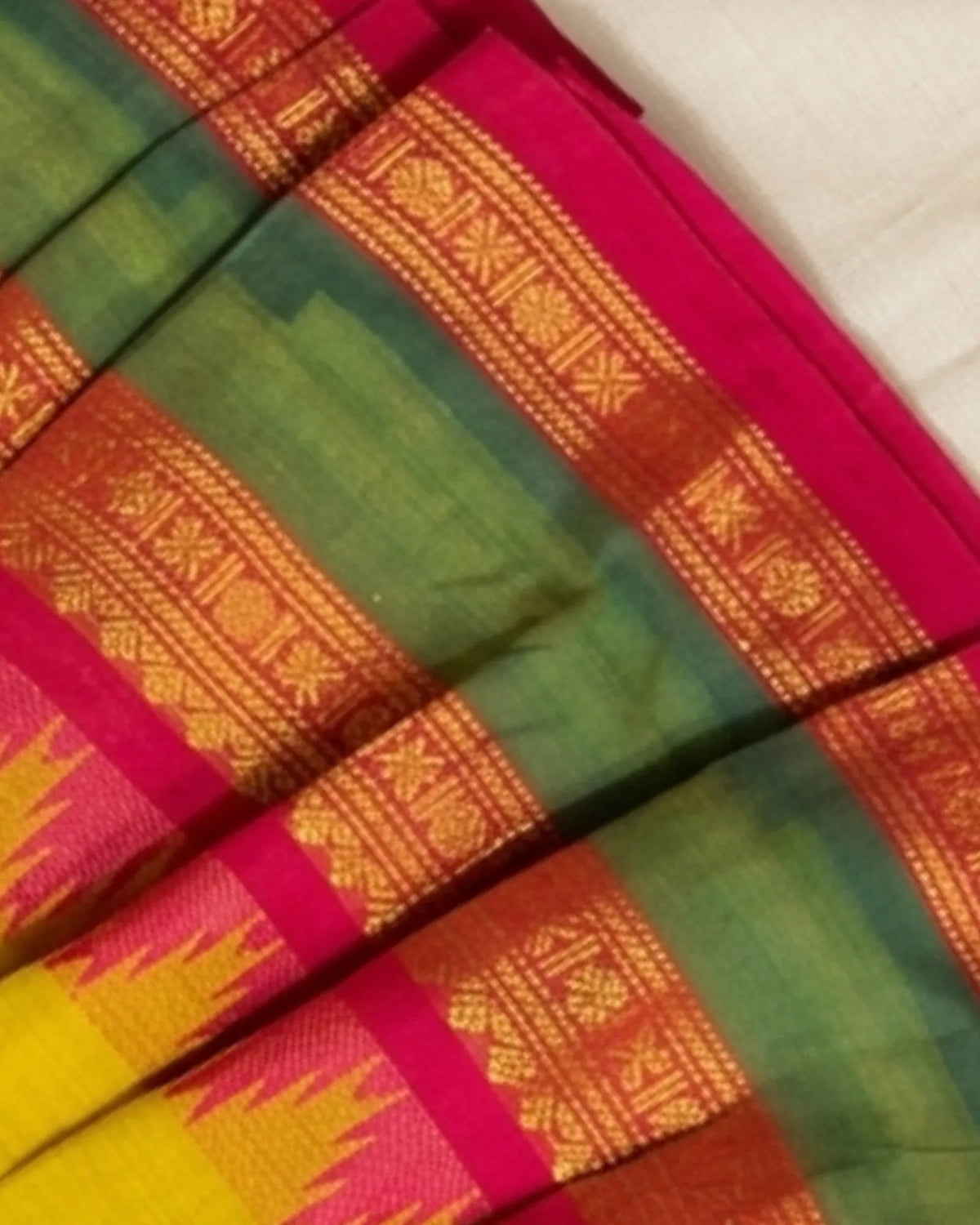 A close-up of a folded traditional Indian saree fabric, showcasing its rich color story of green body, vibrant magenta pink borders, and golden-yellow zari woven patterns.