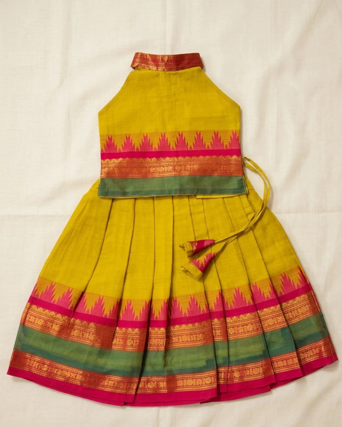 A yellow pleated traditional skirt with a matching sleeveless top, featuring pink, green, and gold patterned borders, laid flat on a white fabric background.