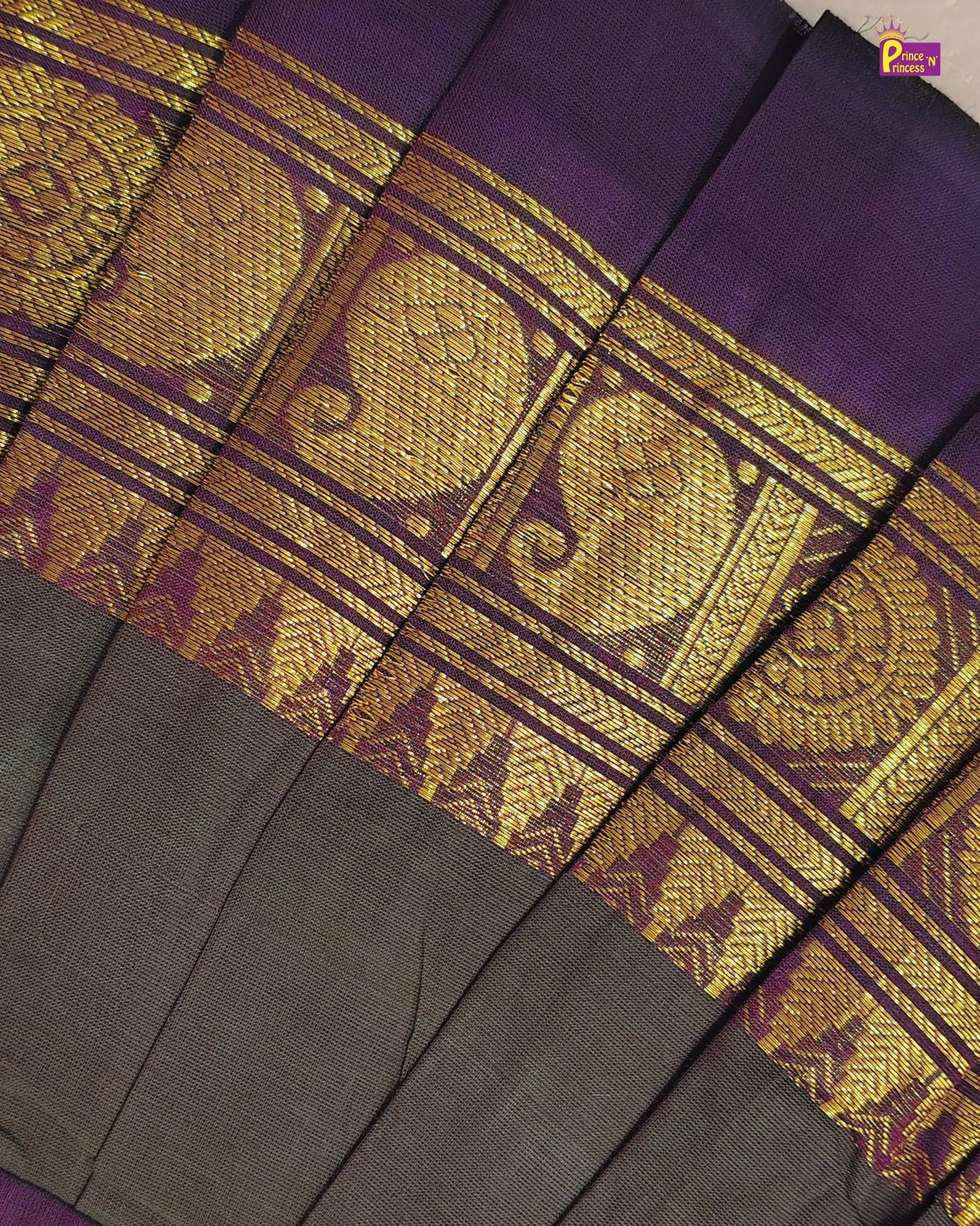 A close-up of a pleated fabric, likely a sari, featuring a deep purple body, a wide metallic gold woven border with traditional motifs, and a dark gray lower section.