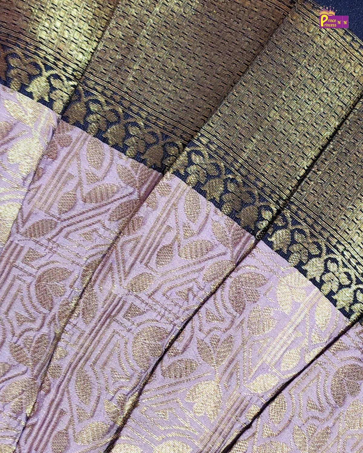 A close-up of a woven fabric, likely a saree, featuring a lavender-purple body with metallic gold floral patterns and a dark navy border with gold zari detailing.