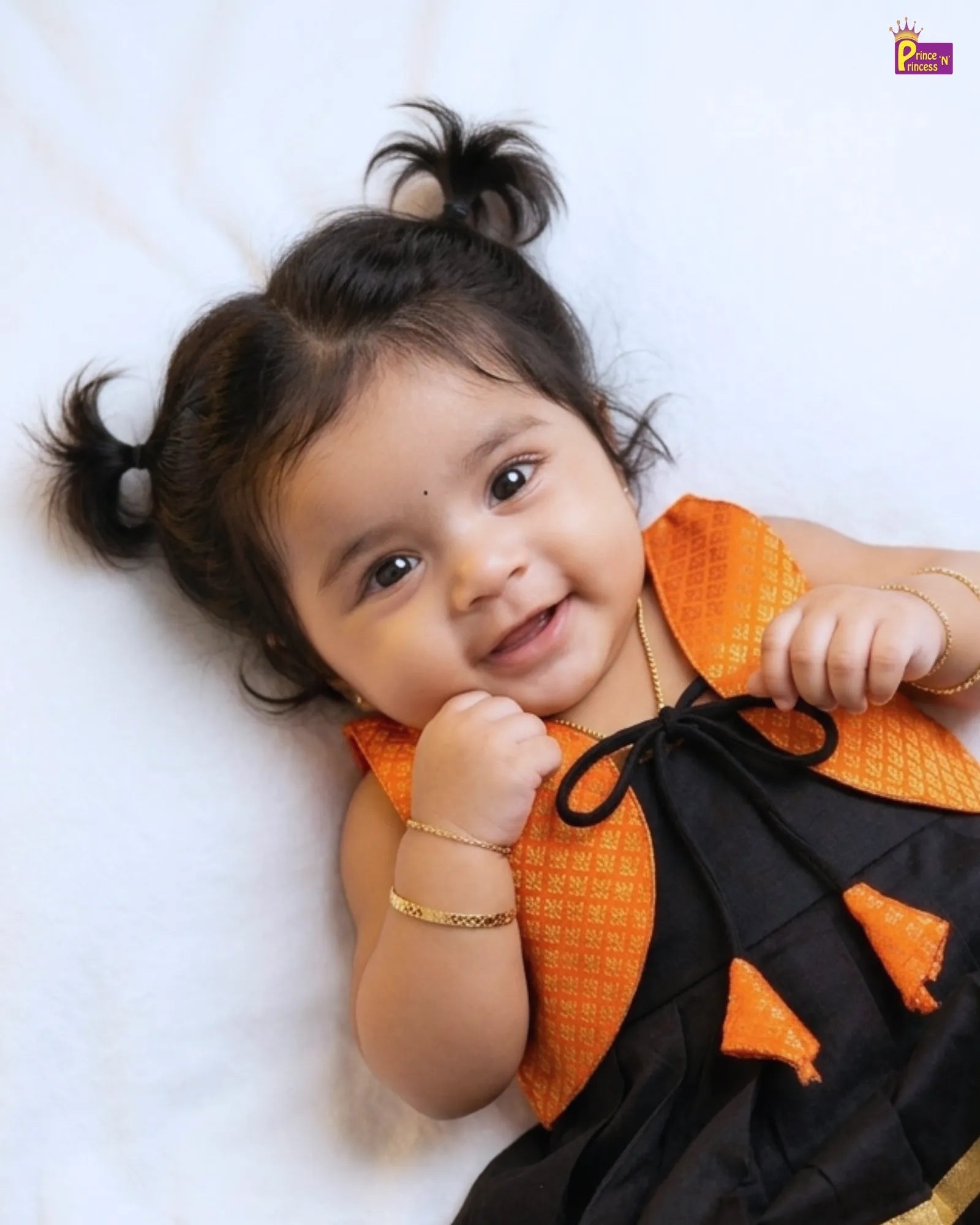 Baby wearing an orange and black traditional outfit on a white background