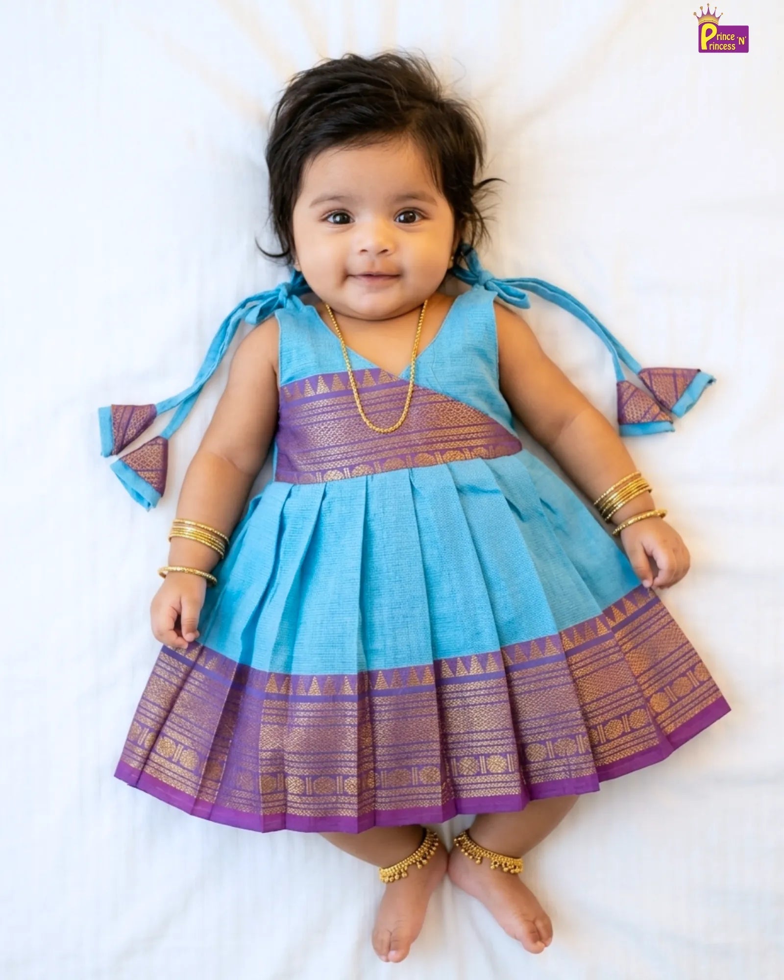 Baby wearing a blue and purple traditional outfit on a white background