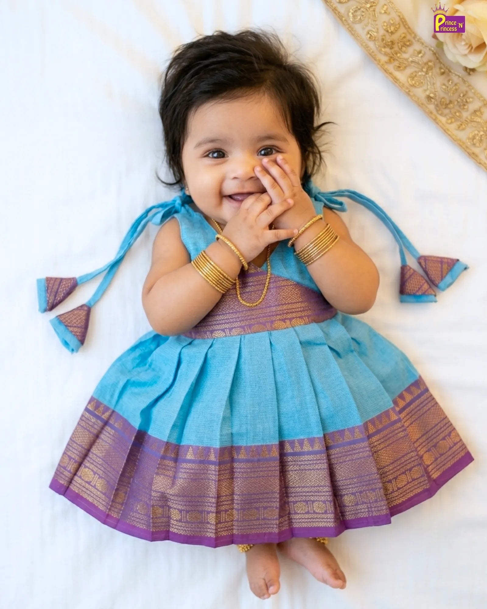 Baby in a blue and purple traditional outfit with gold jewelry on a white background