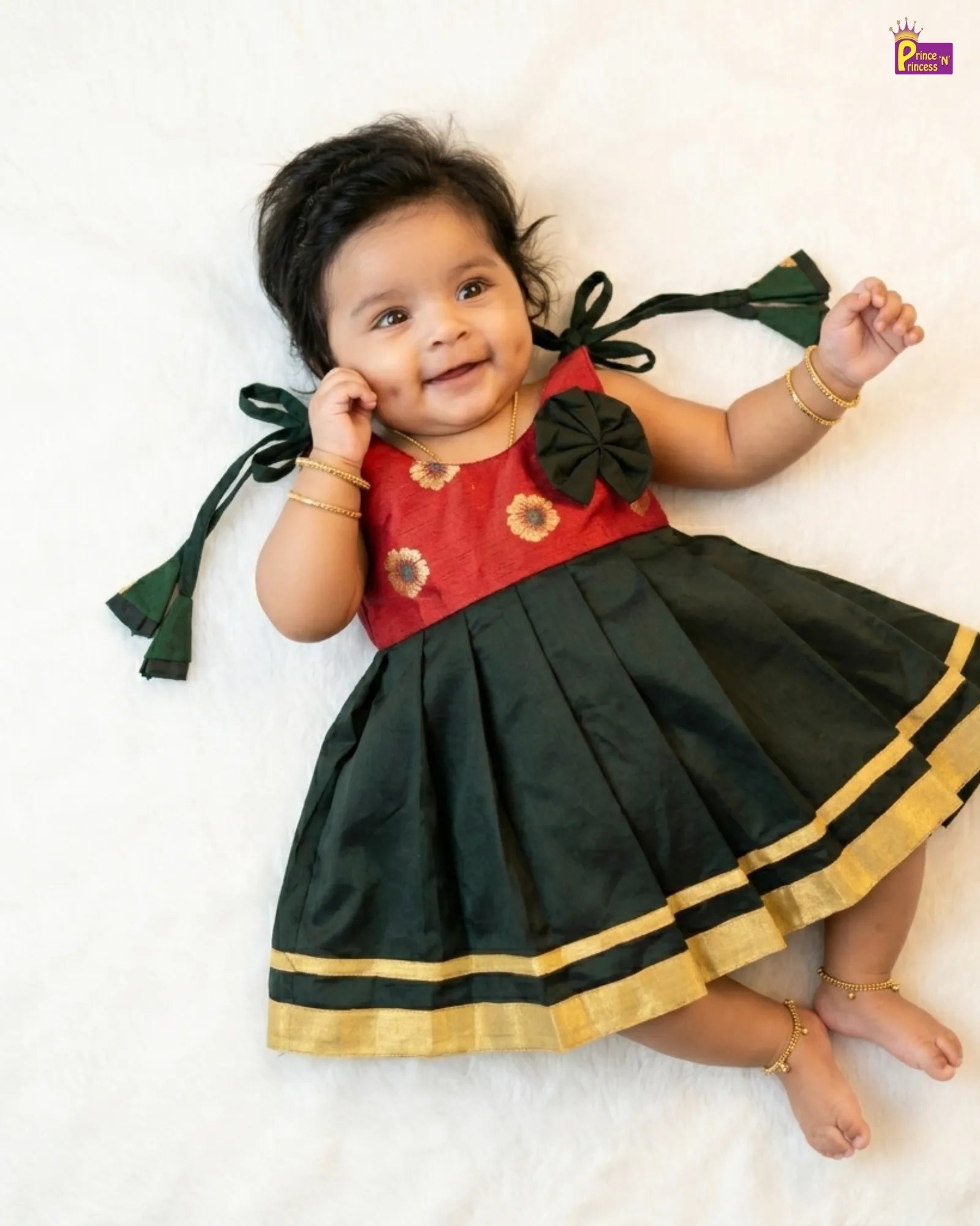 Baby wearing a red and green traditional outfit with gold trim on a white background
