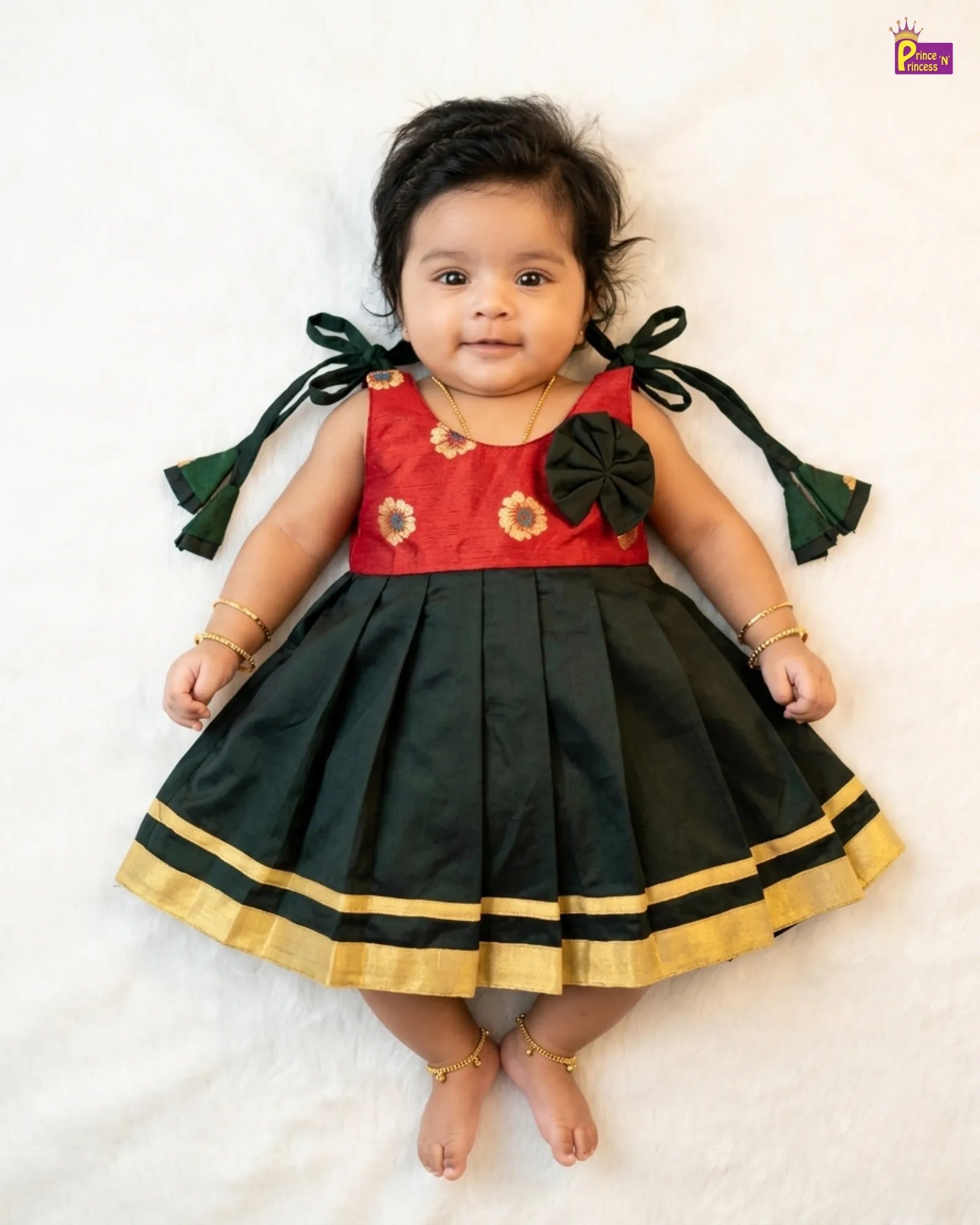 Baby wearing a red and black traditional outfit with gold trim on a white background