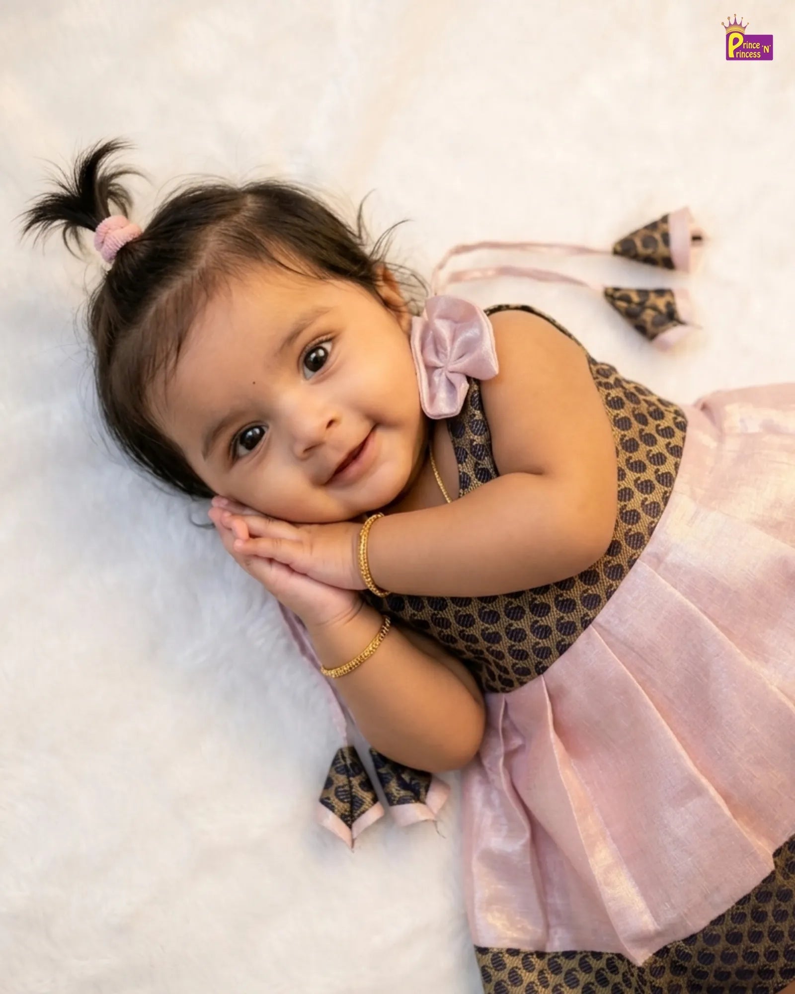 Child wearing a patterned dress with a pink bow and skirt, lying on a white surface.